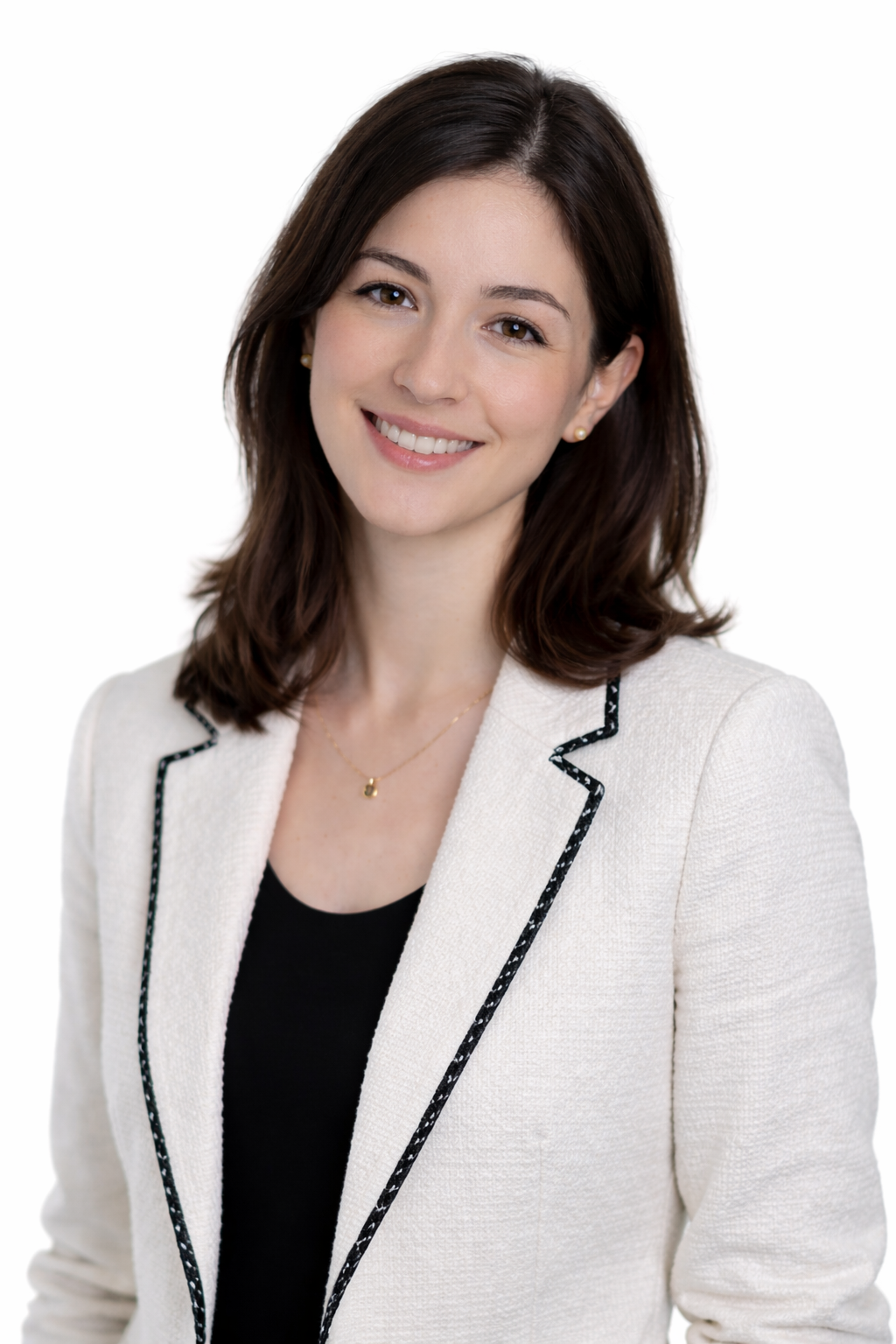 A woman with shoulder-length brown hair, smiling, wearing a white blazer with black patterned trim, a black top, and small pearl earrings, standing against a plain white background.