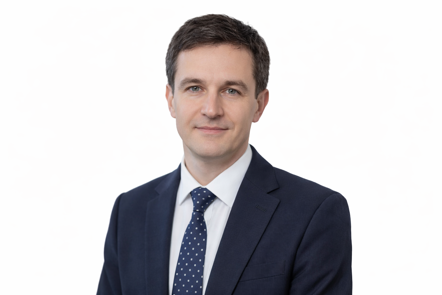 A professional man in a navy suit, white shirt, and navy polka dot tie, looking at the camera with a slight smile, against a plain white background.