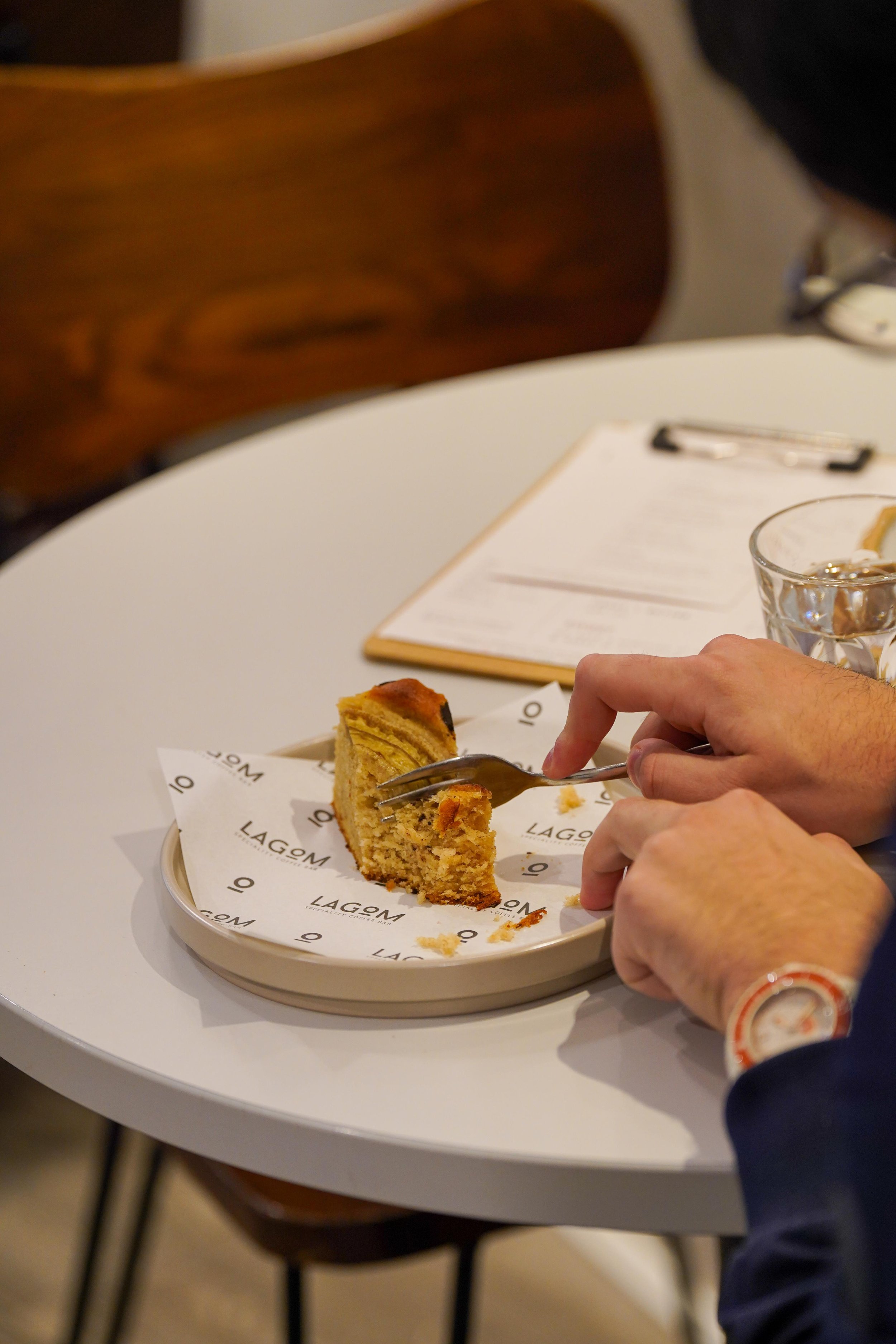 Person eating a slice of cake on a white plate at a restaurant table.