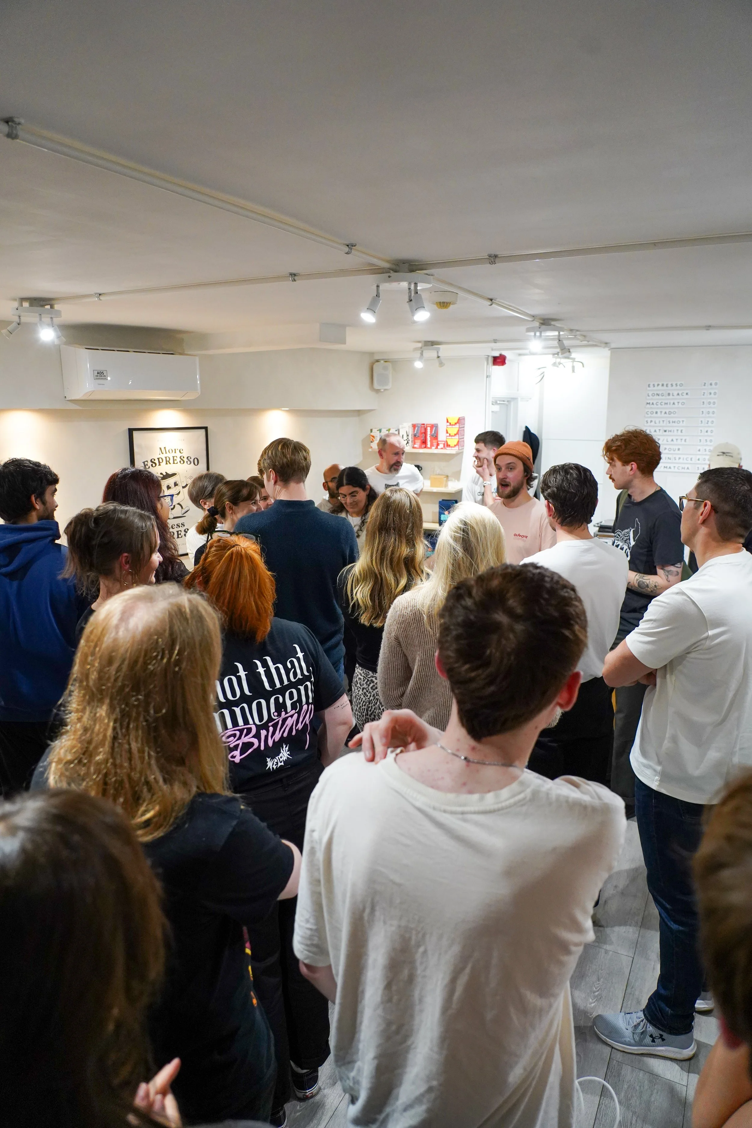 People gathering in a coffee shop, some are talking to baristas behind the counter, wait for orders, and socializing.