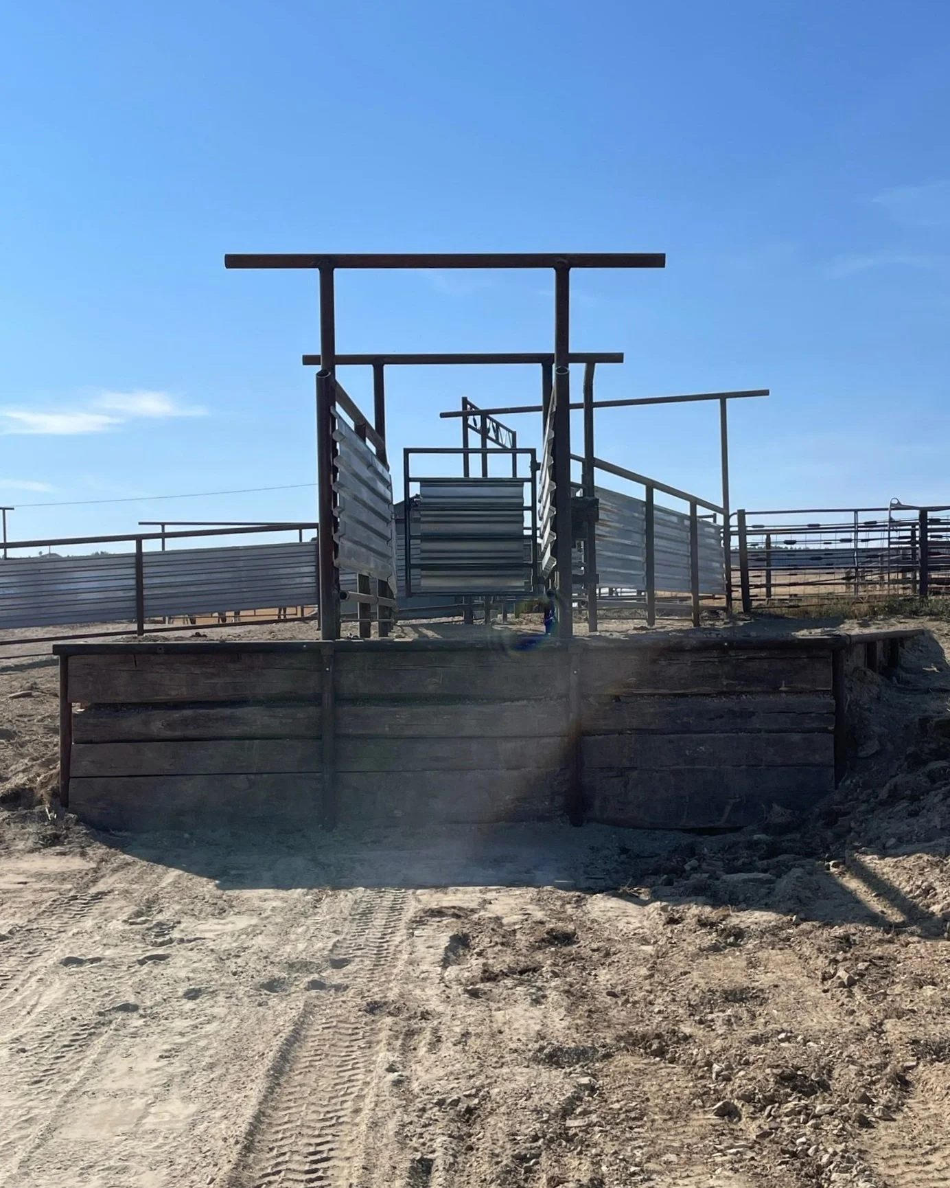 Empty livestock squeeze chute and corral on dirt ground with clear blue sky. Built by Fiddler Creek Design in Upton, WY