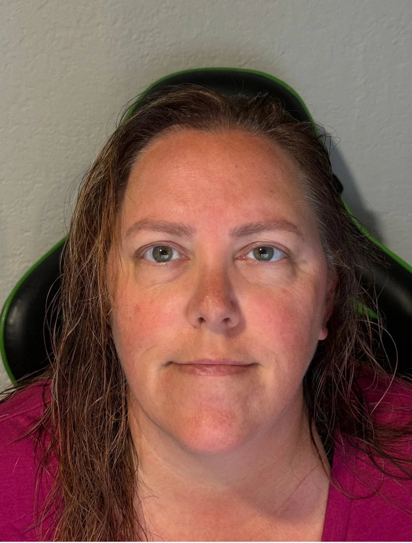 Person with wet hair in pink shirt sitting on a chair, looking at the camera.