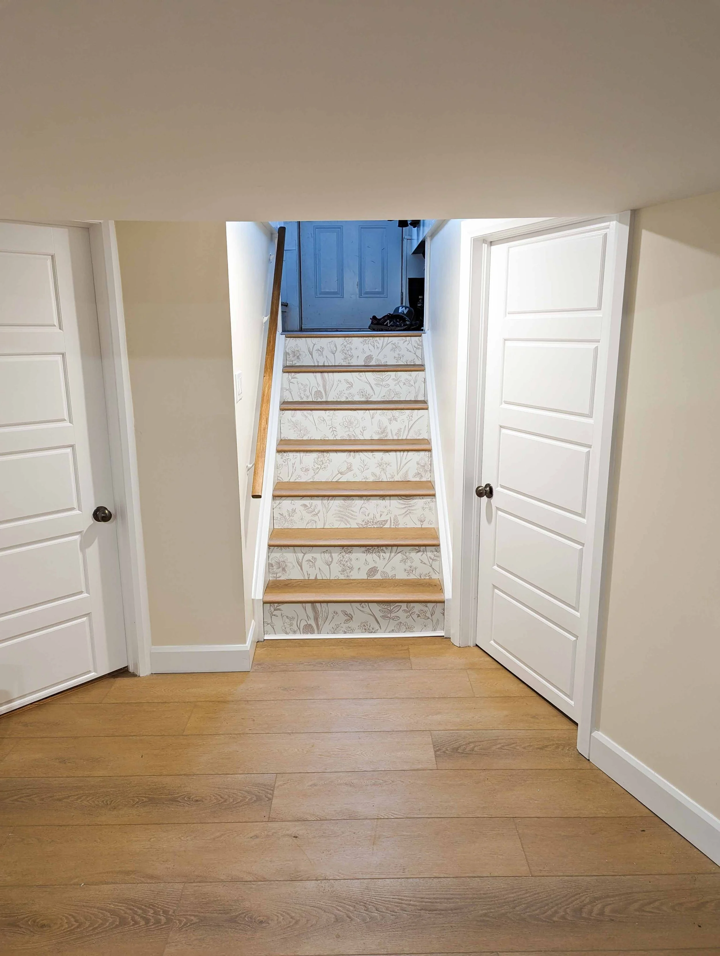 Interior view of a staircase leading to an upper door, with two white paneled closet doors on either side, light-colored walls, and wood flooring.