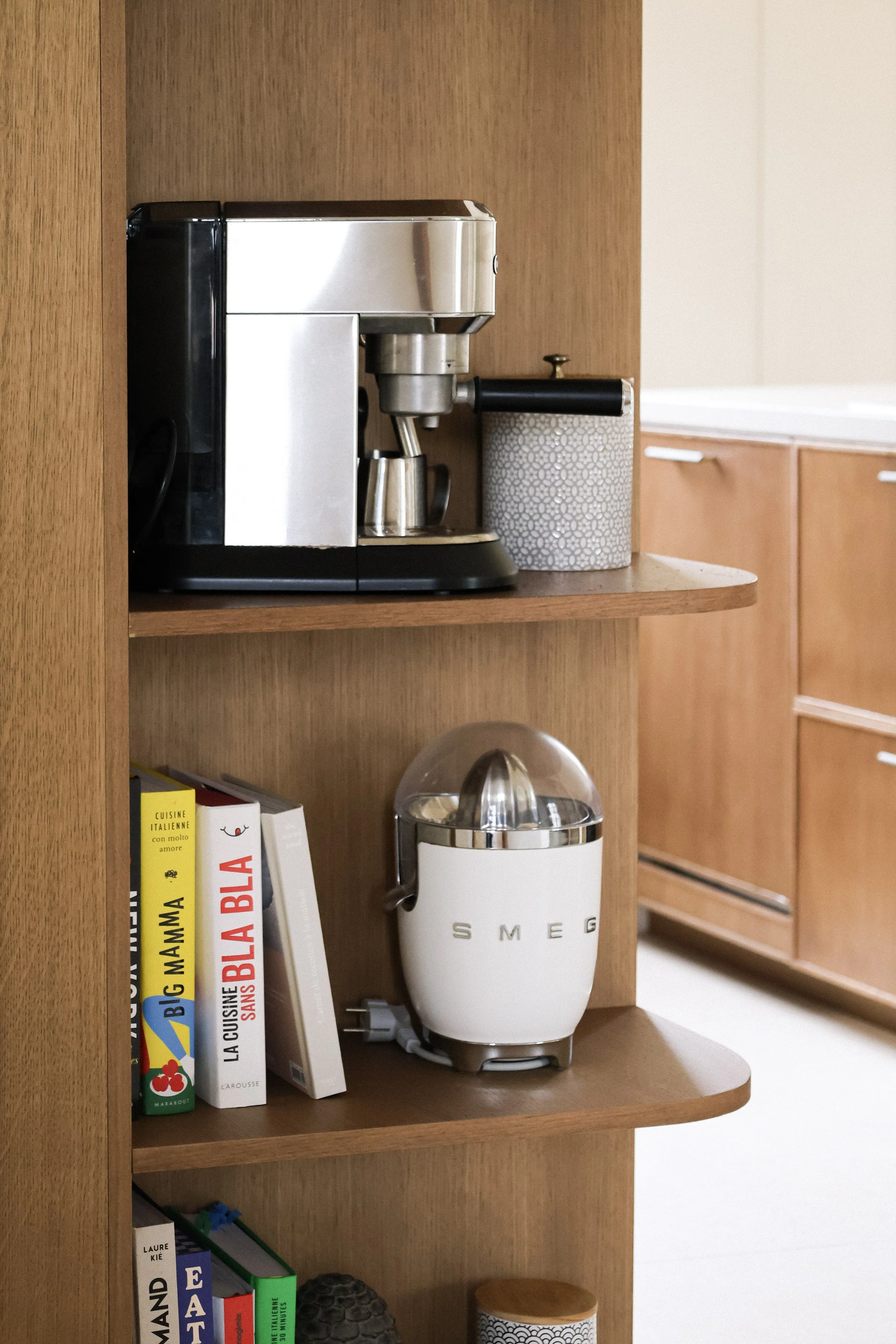Étagère en bois avec une machine à café espresso en haut et un robot SMEG blanc en dessous, accompagnés de livres de cuisine.
