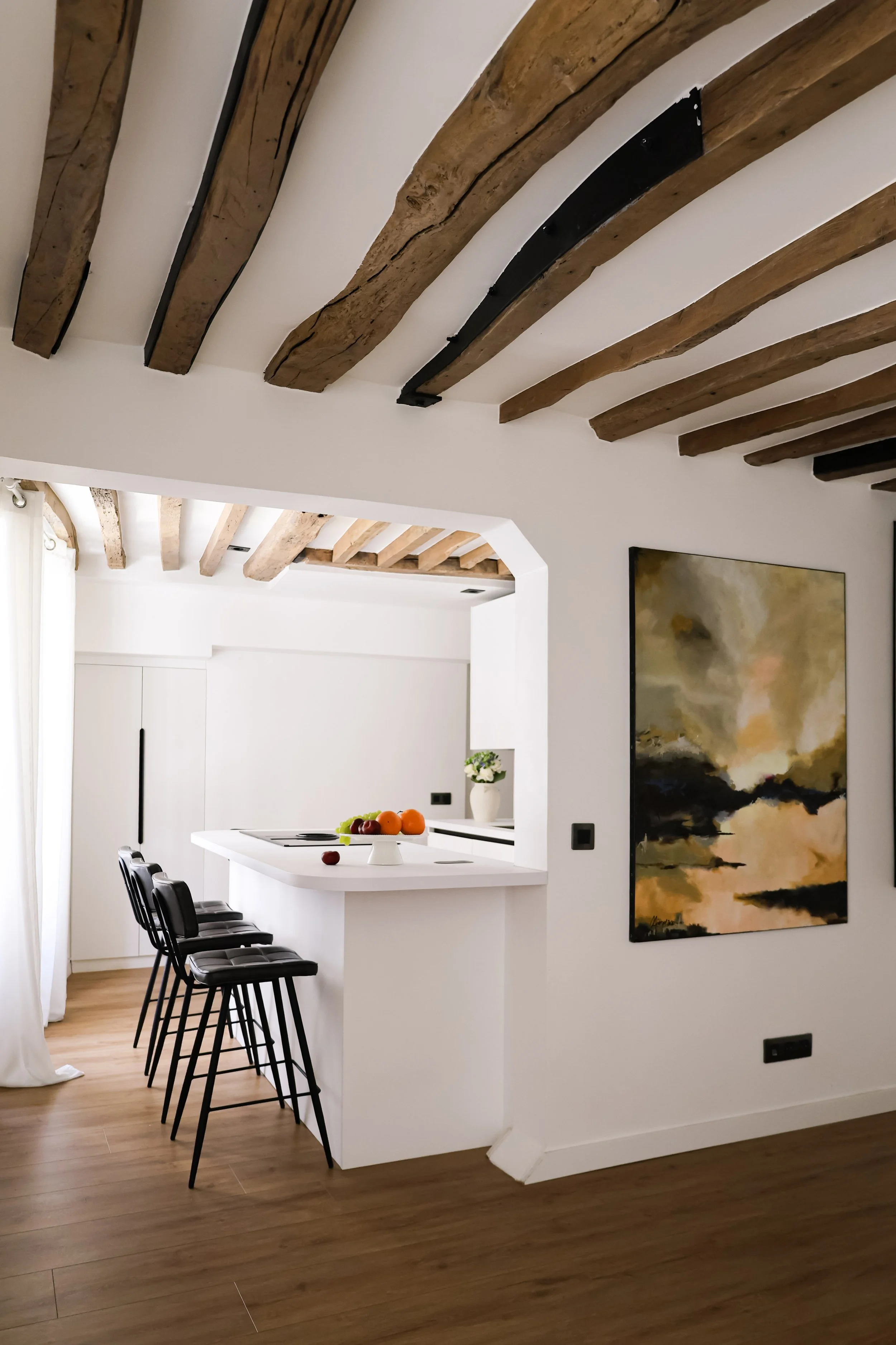 Architecture d’intérieur contemporaine minimaliste france : design sur mesure, décoration haut de gamme, gestion de chantier, conception. Intérieur moderne d'une cuisine avec plafond en poutres en bois, comptoir blanc, chaises hautes noires,