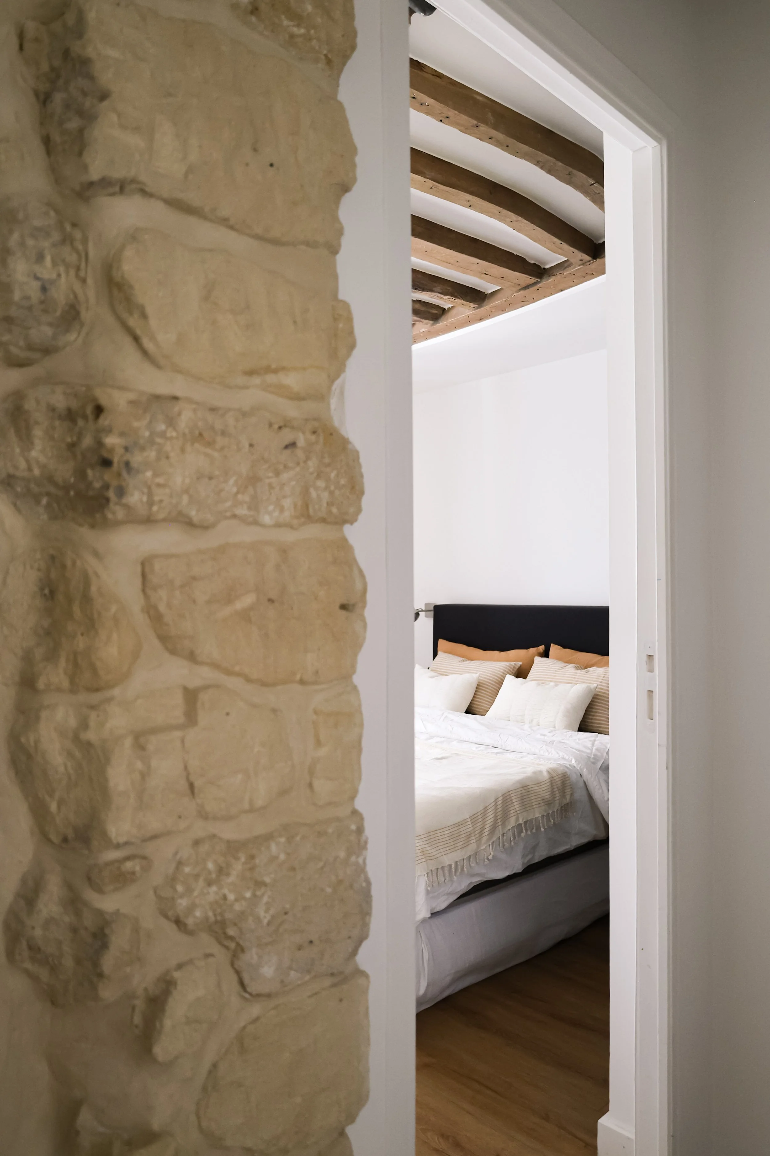 Une chambre à coucher vue partiellement à travers une porte, avec un lit, des coussins et un plafond en bois.