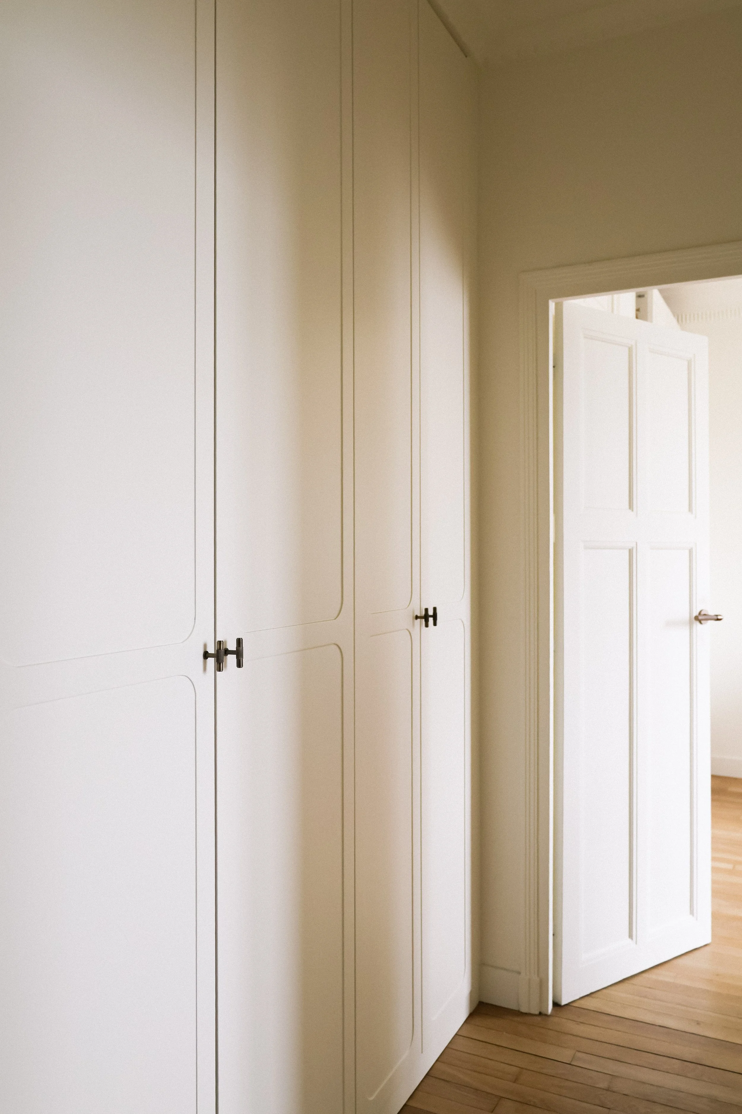 Une pièce avec des placards blancs sur le mur et une porte ouverte à droite, avec un sol en bois.