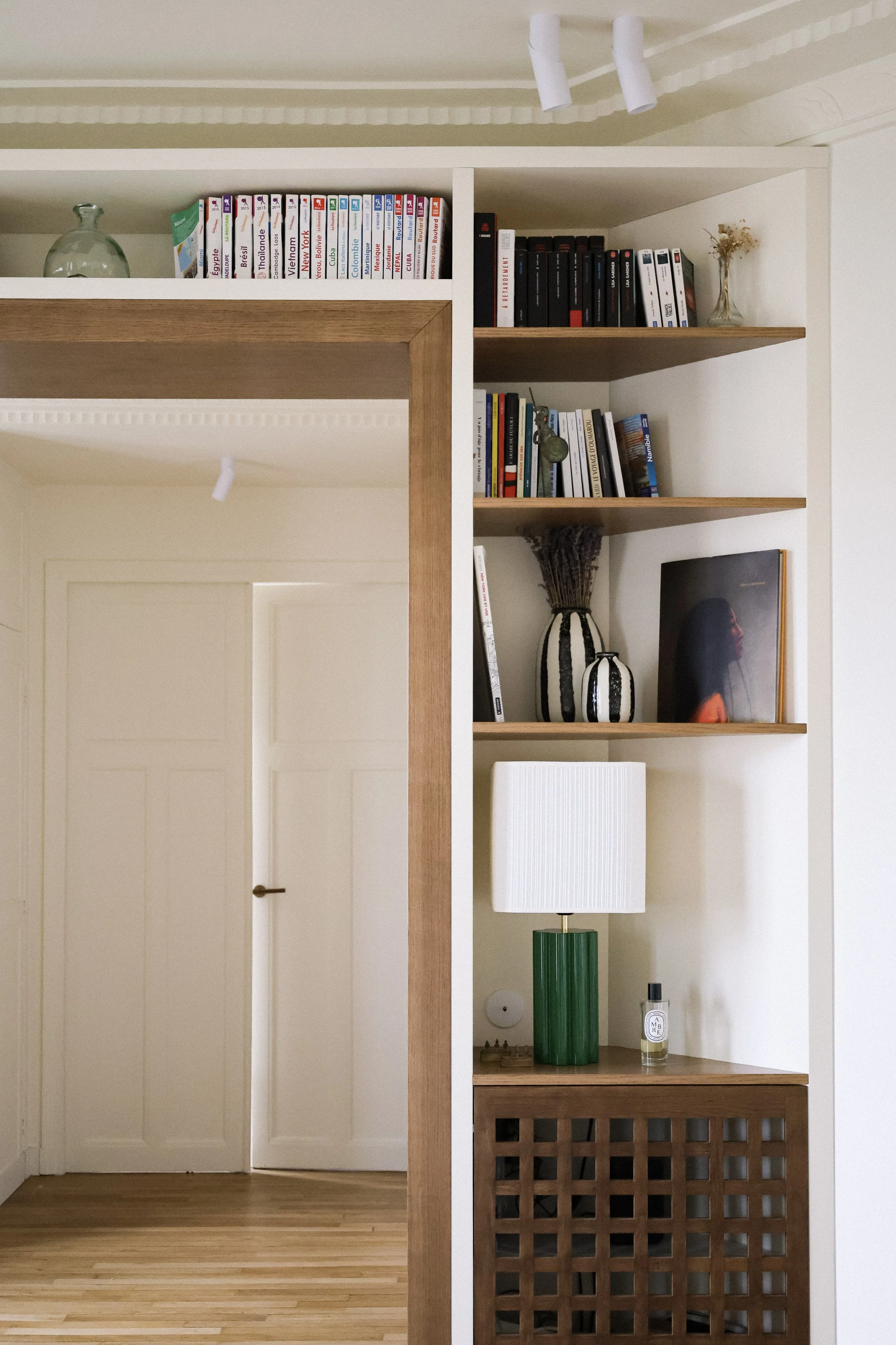 meuble d'angle avec étagères en bois, décor avec livres, vases, lampe verte et blanche, et un livre posé verticalement.