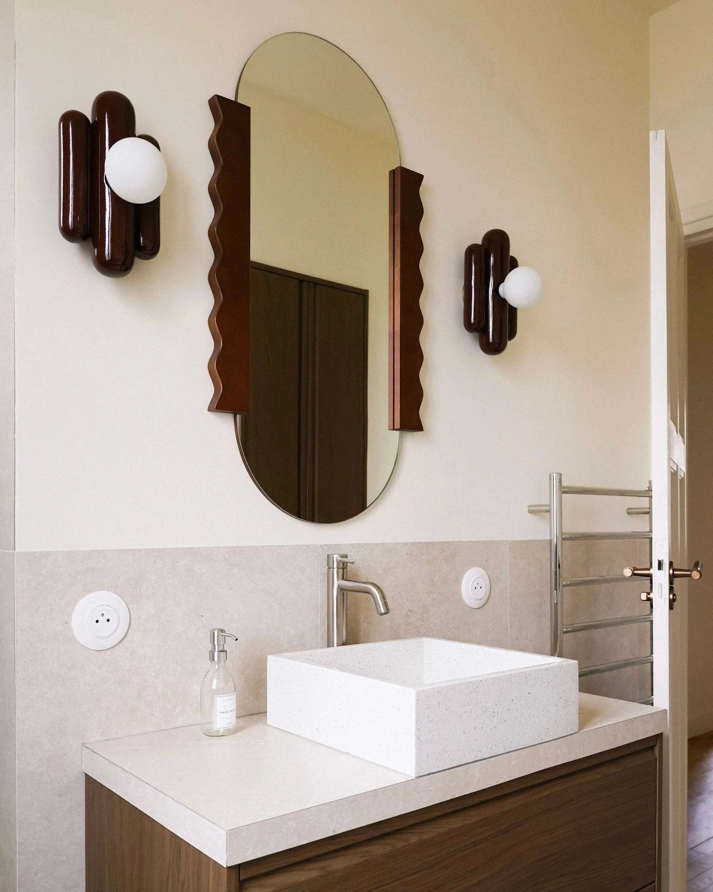 Architecture d’intérieur contemporaine minimaliste france : design sur mesure, décoration haut de gamme, gestion de chantier, conception Lavabo en marbre blanc dans une salle de bain moderne avec un miroir ovale, deux appliques murales en bois foncé