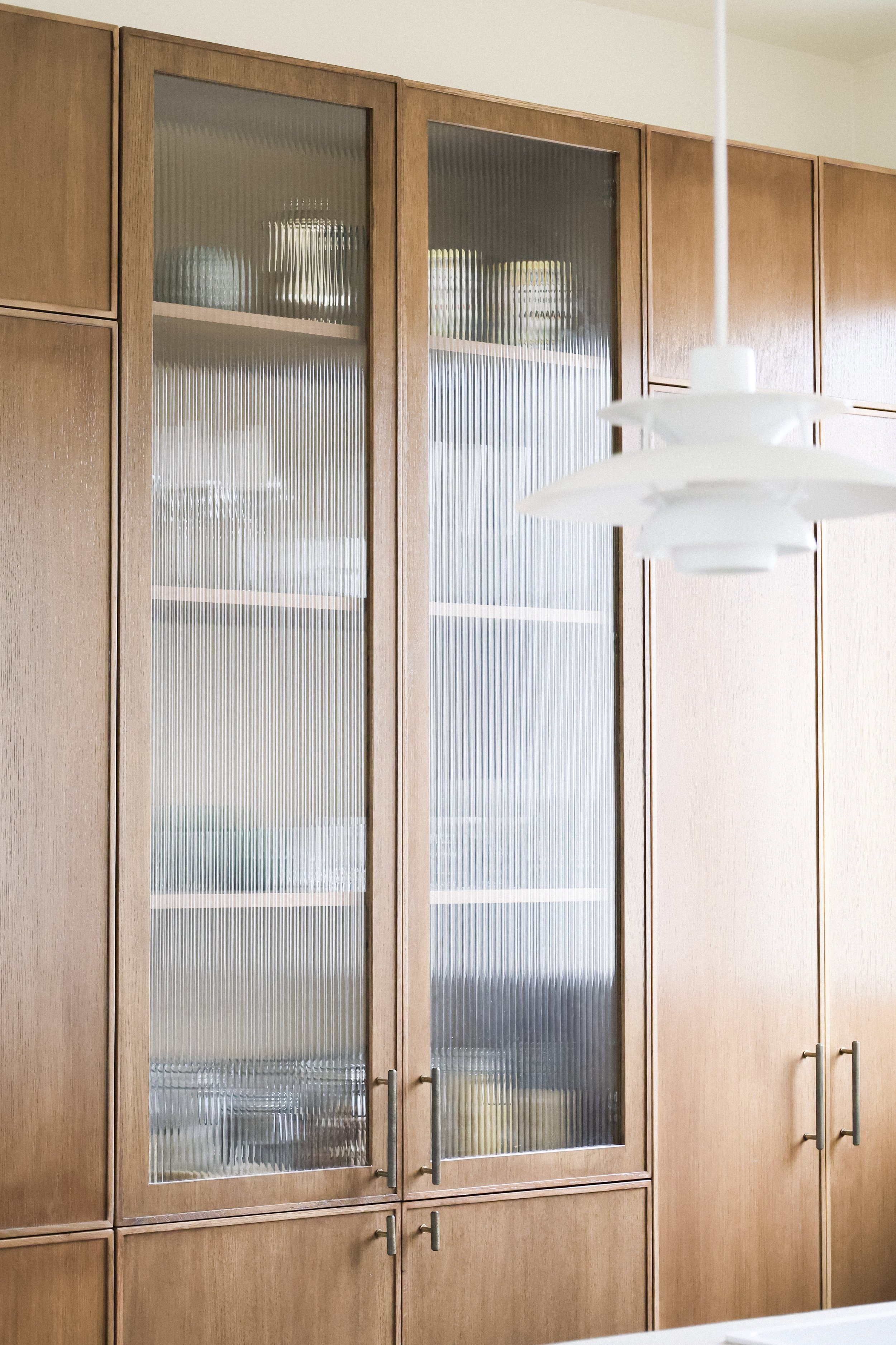 Armoire en bois avec portes en verre dépoli, dans une cuisine, avec un plafonnier blanc suspendu.