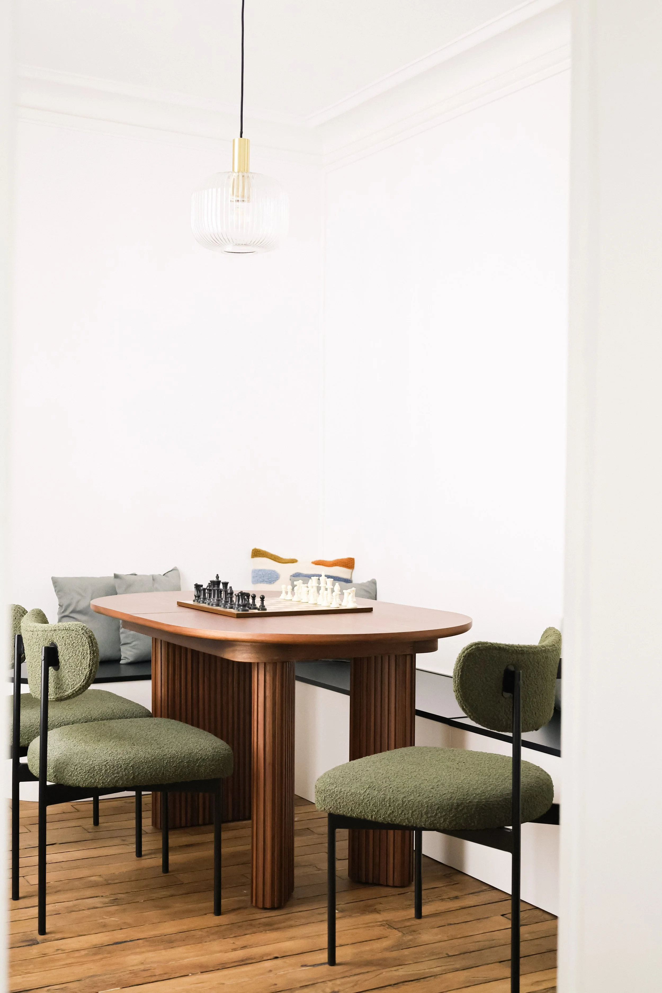 Salle à manger avec table en bois, chaises vertes, peinture murale abstraite, et lampe suspendue moderne.