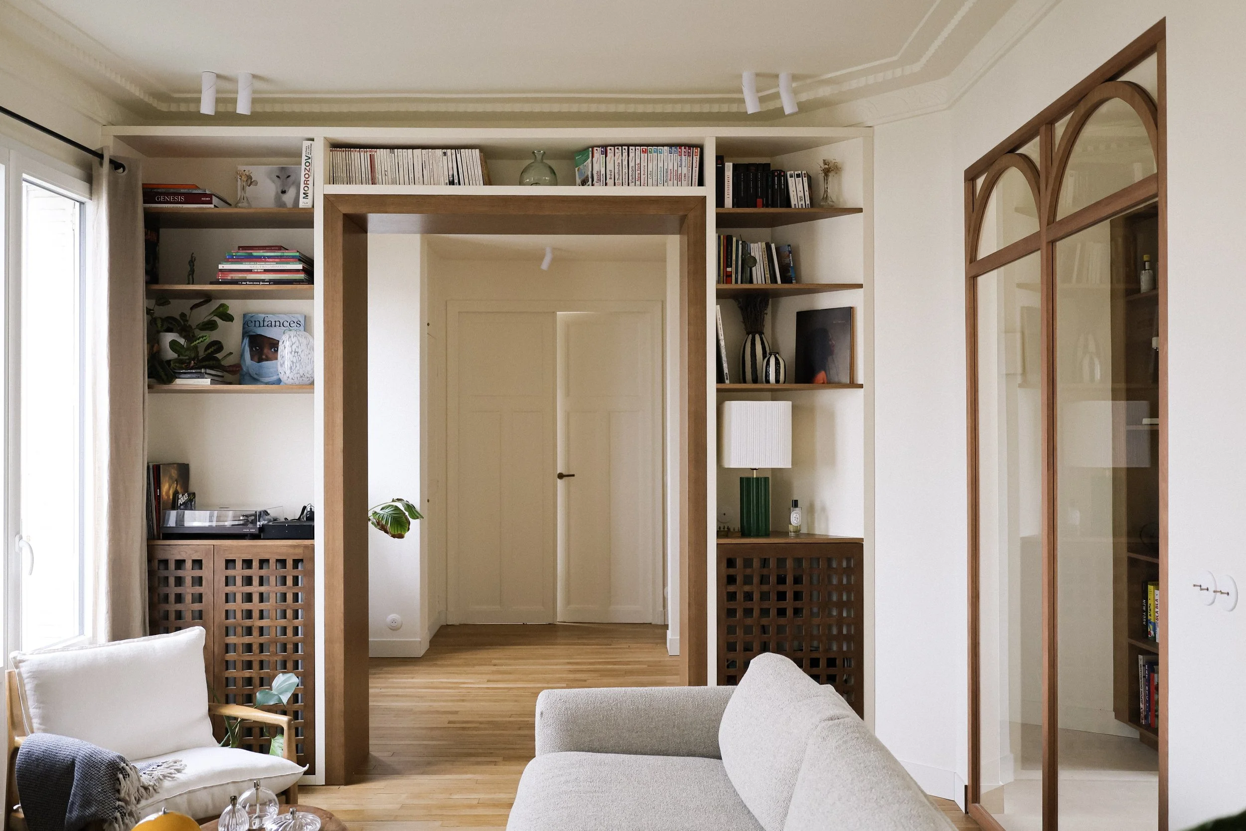 Intérieur d'un salon moderne avec étagères en bois, canapé beige, mobilier en bois, livres, plantes et décorations.