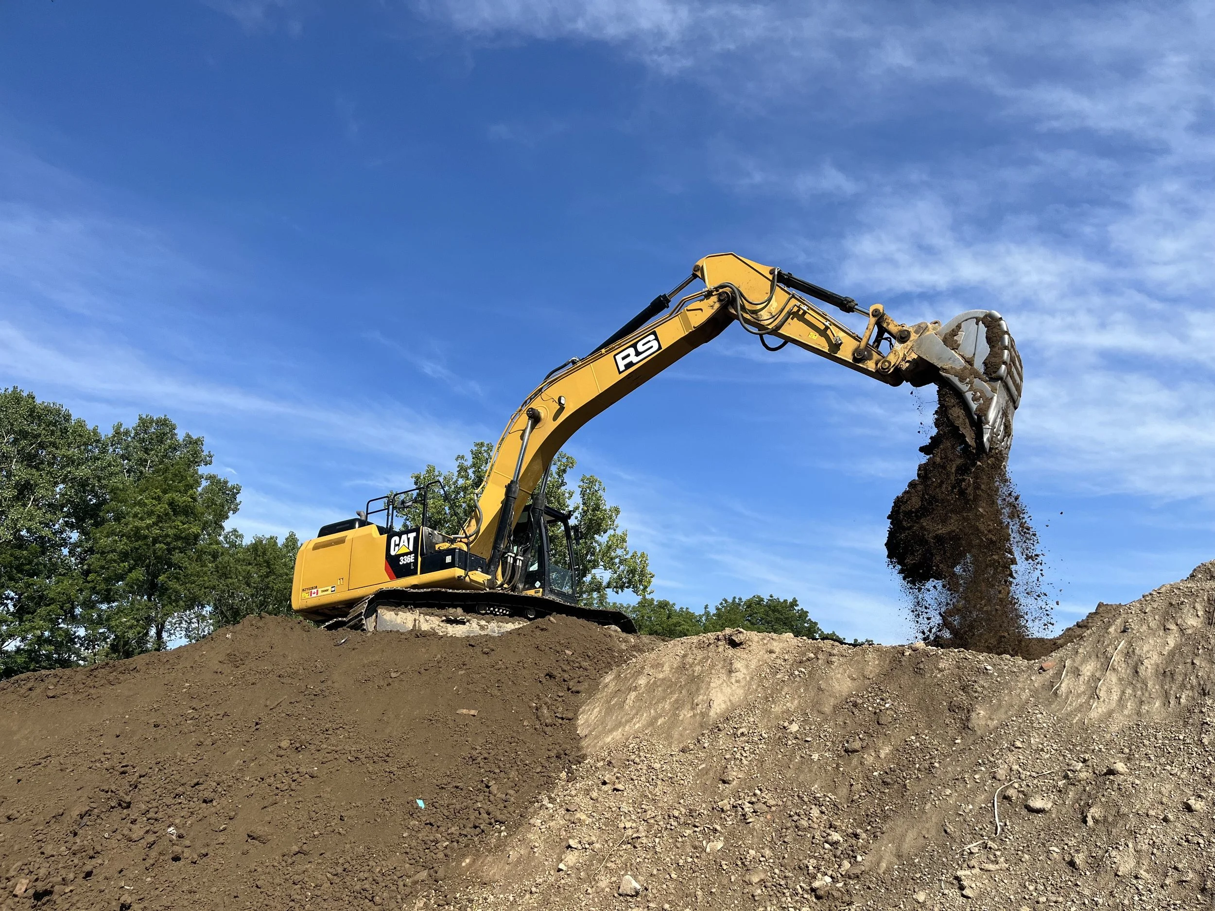 Yellow industrial front loader parked on a dirt surface with bare trees in the background.
