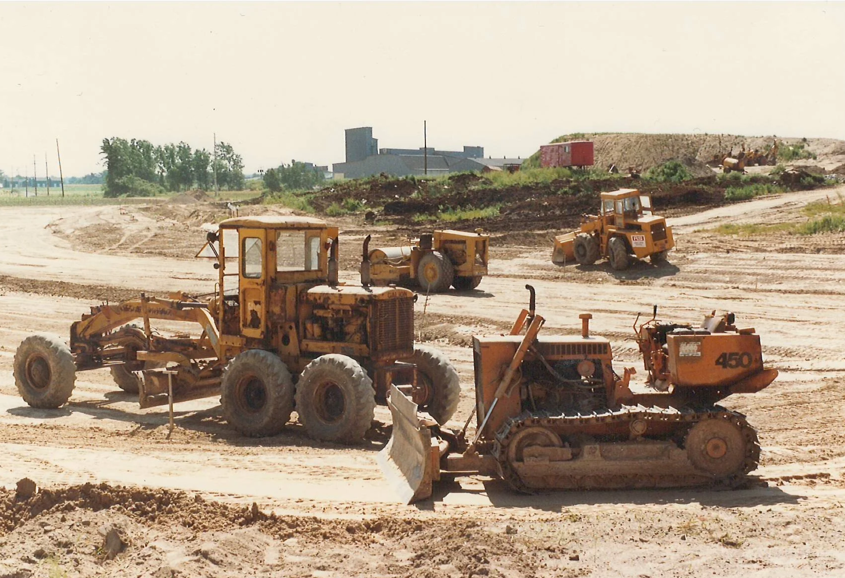 Vintage red excavator on muddy terrain with a label "ROBERT SIMON CONSTRUCTION" and "LS98". Weathered appearance suggests an old photograph.