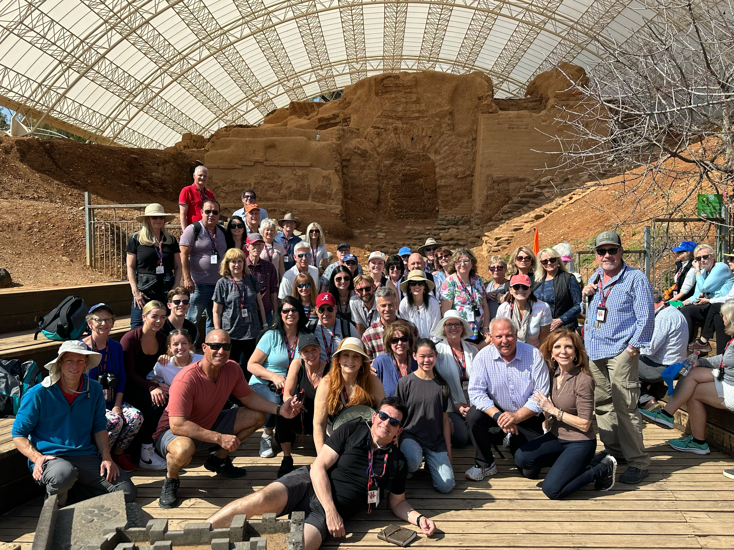 A group of people posing for a photo at an archaeological site with ruins and a canopy overhead.