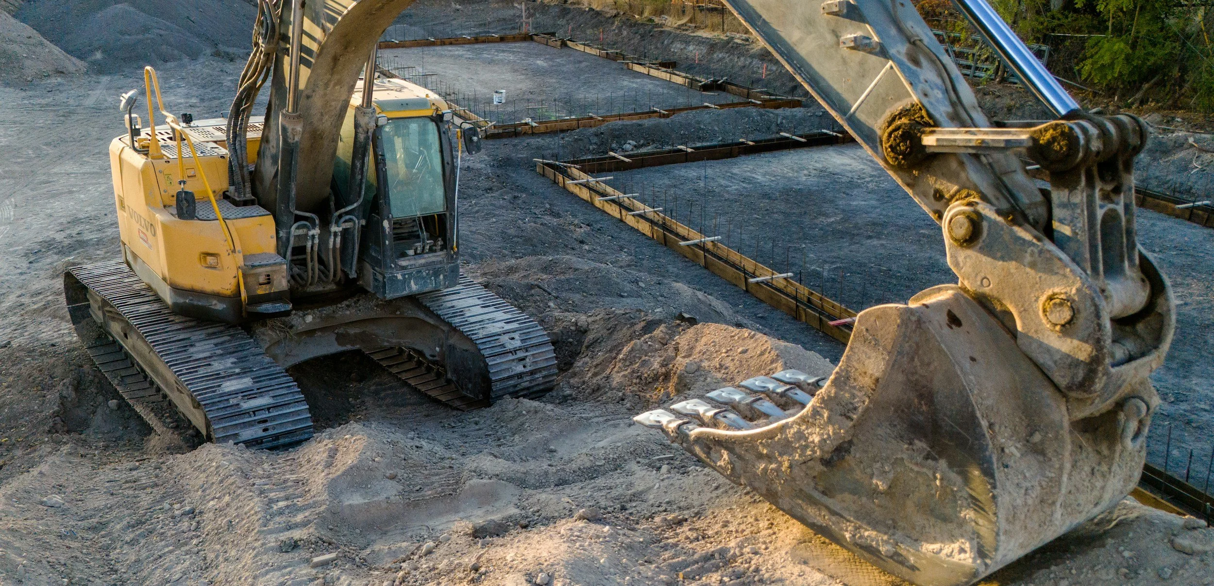 Excavator on construction site with dirt terrain and foundation outlines