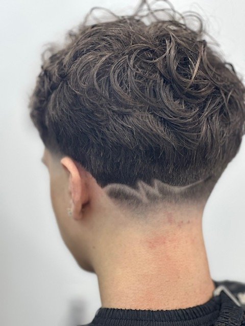 Curly hairstyle with shaved zigzag design on the nape of the neck.
