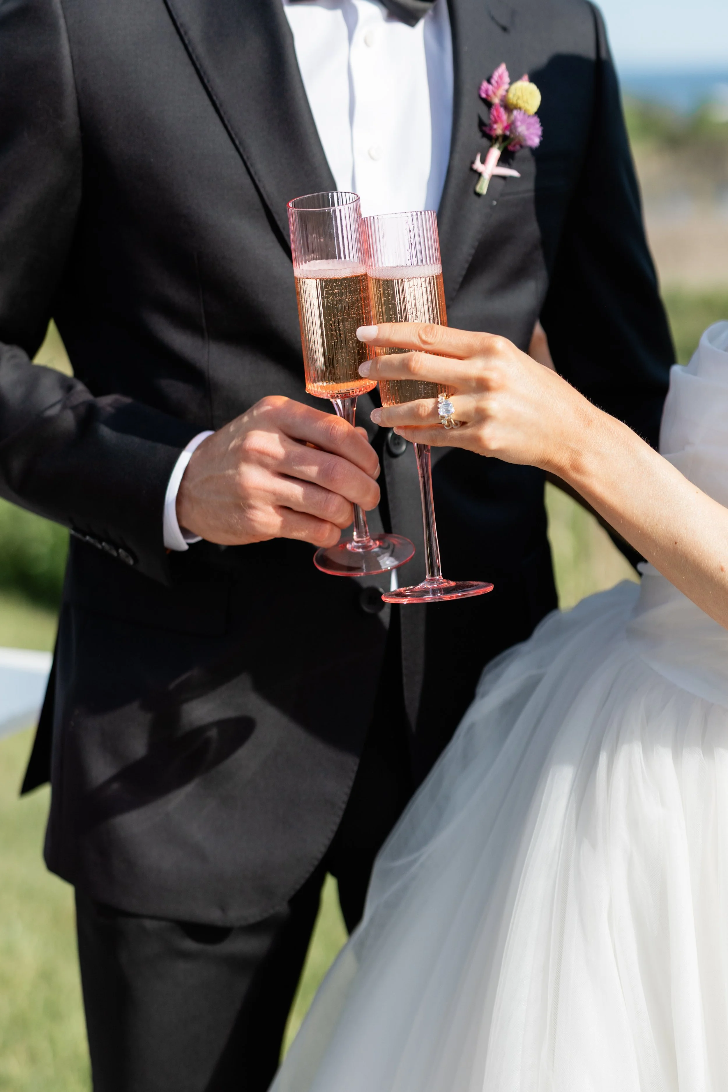 Bride and groom at wedding celebration, toasting with glasses of champagne outdoors.