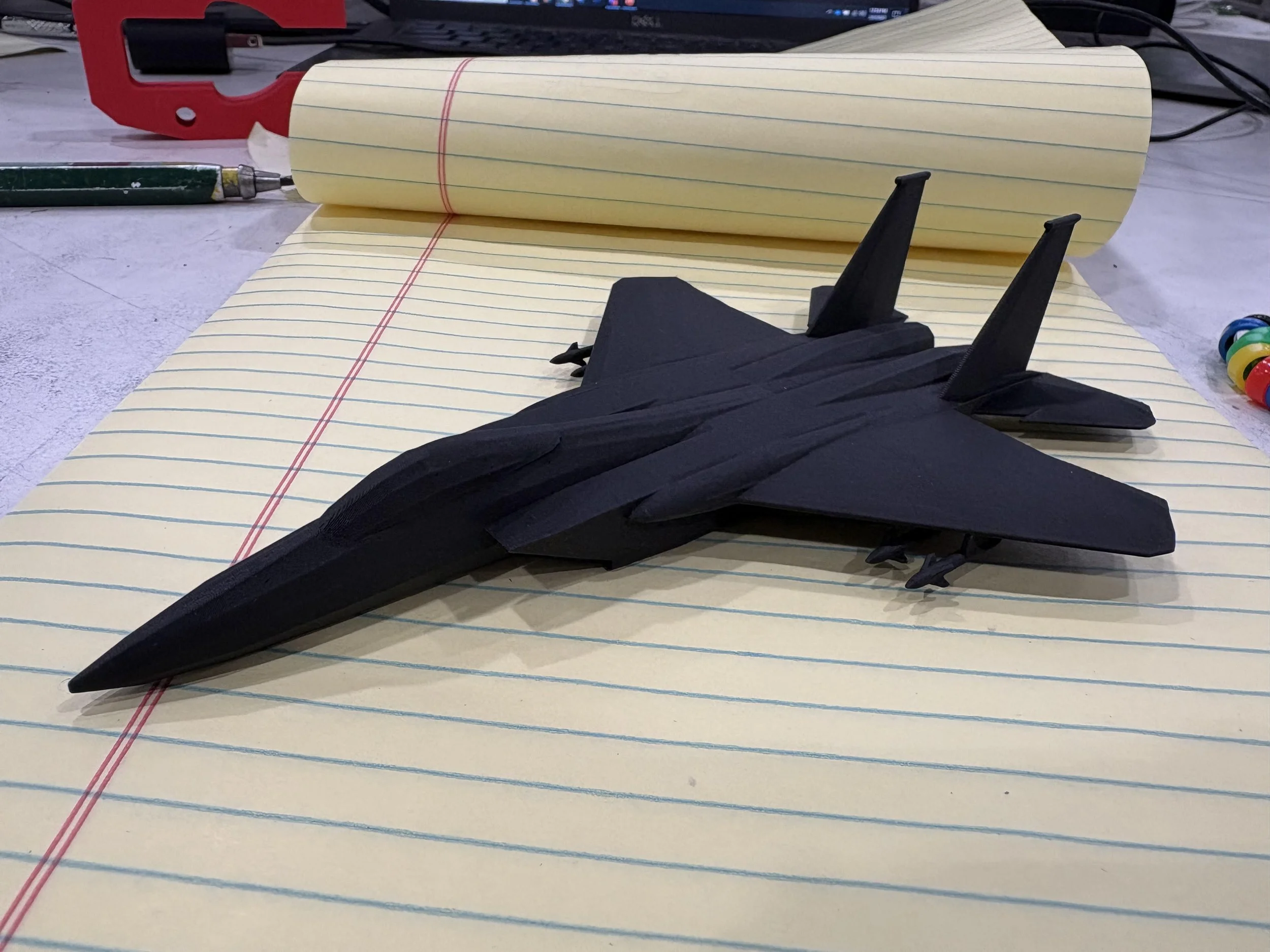A 3D printed model of a black F-15 on a yellow legal pad.