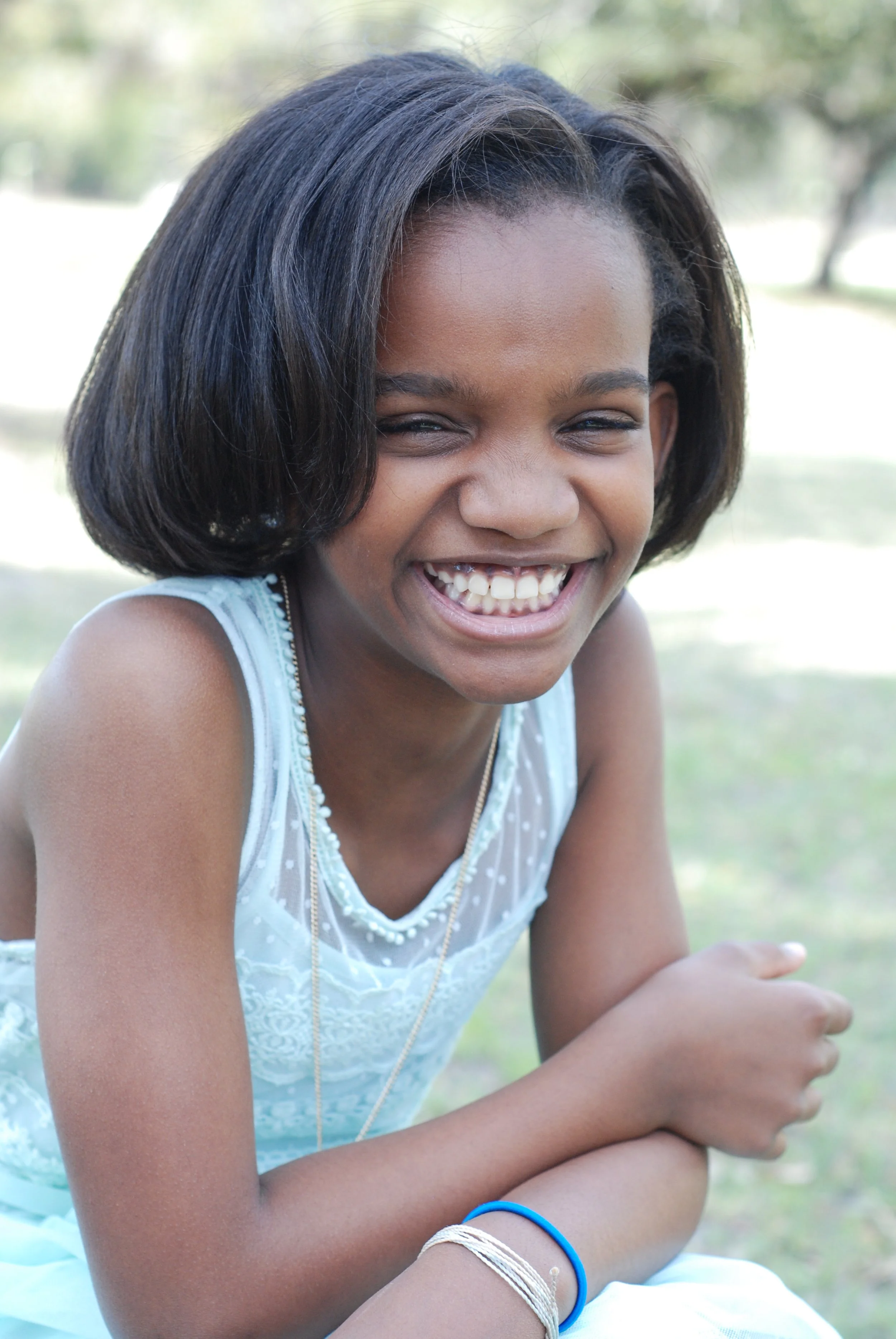 Young girl with short black hair laughing outdoors in a park setting