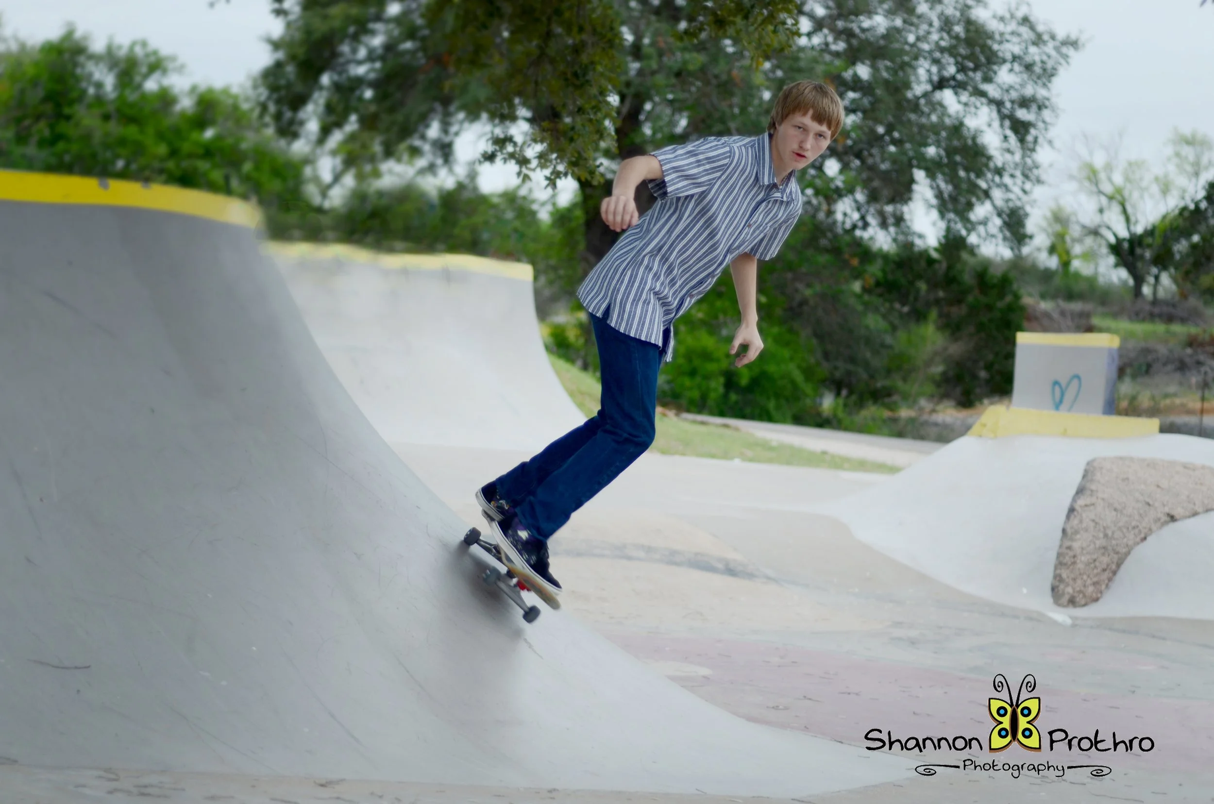 A young boy skateboarding on a concrete ramp at a skate park outdoors with trees in the background.