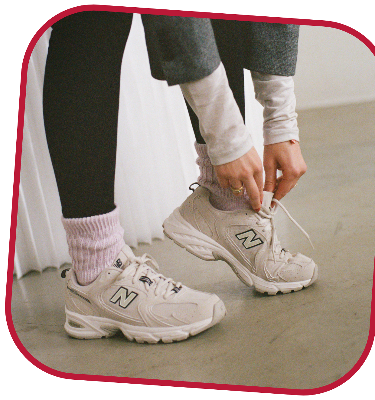 Taylor tying her New Balance sneakers wearing black leggings, pink socks, a white shirt, and a grey blazer.