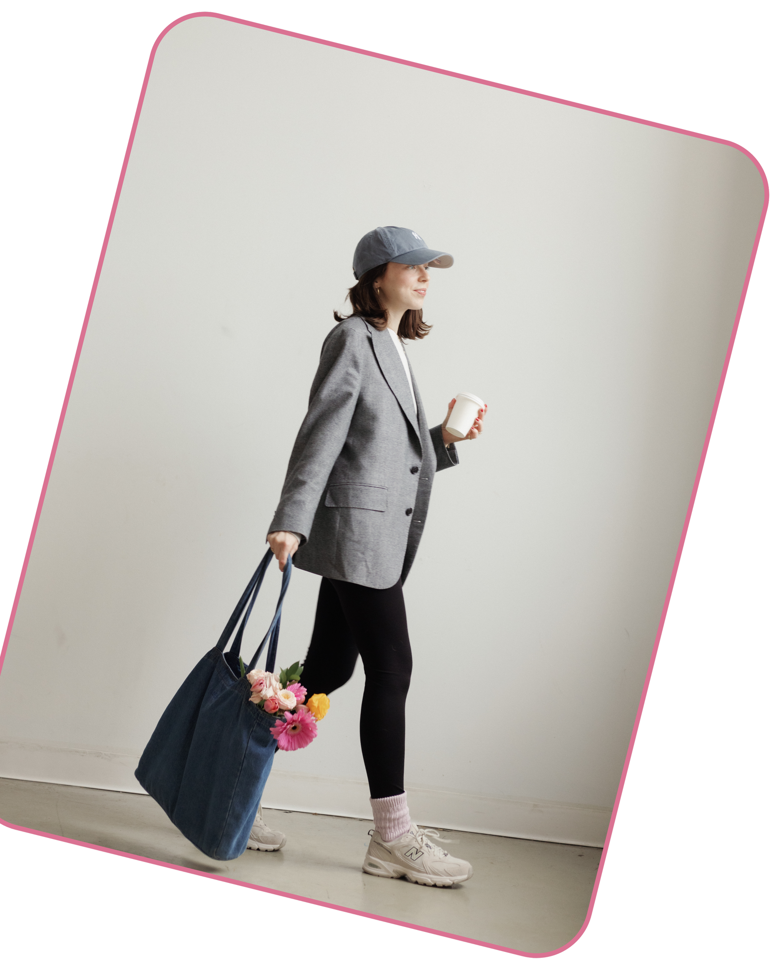 Taylor walks with a coffee cup in left hand and a denim tote with flowers in right hand. Taylor is dressed in a gray blazer, black leggings, white sneakers, a grey baseball cap, and pink socks.