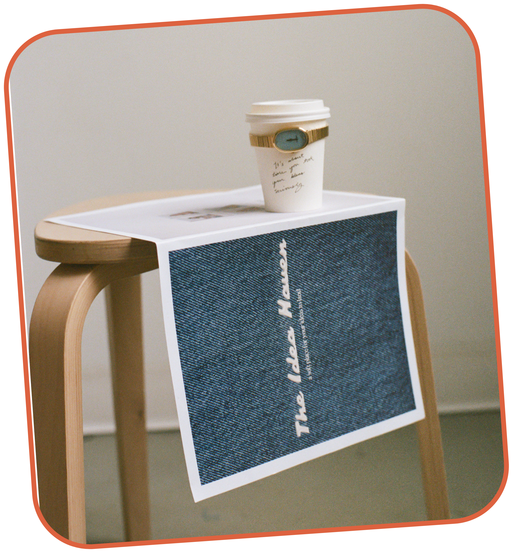 A wooden stool with a large dark blue and white printed brand newspaper draped over the side, with a white paper coffee cup on top and a gold and sky blue watch wrapped around the cup.