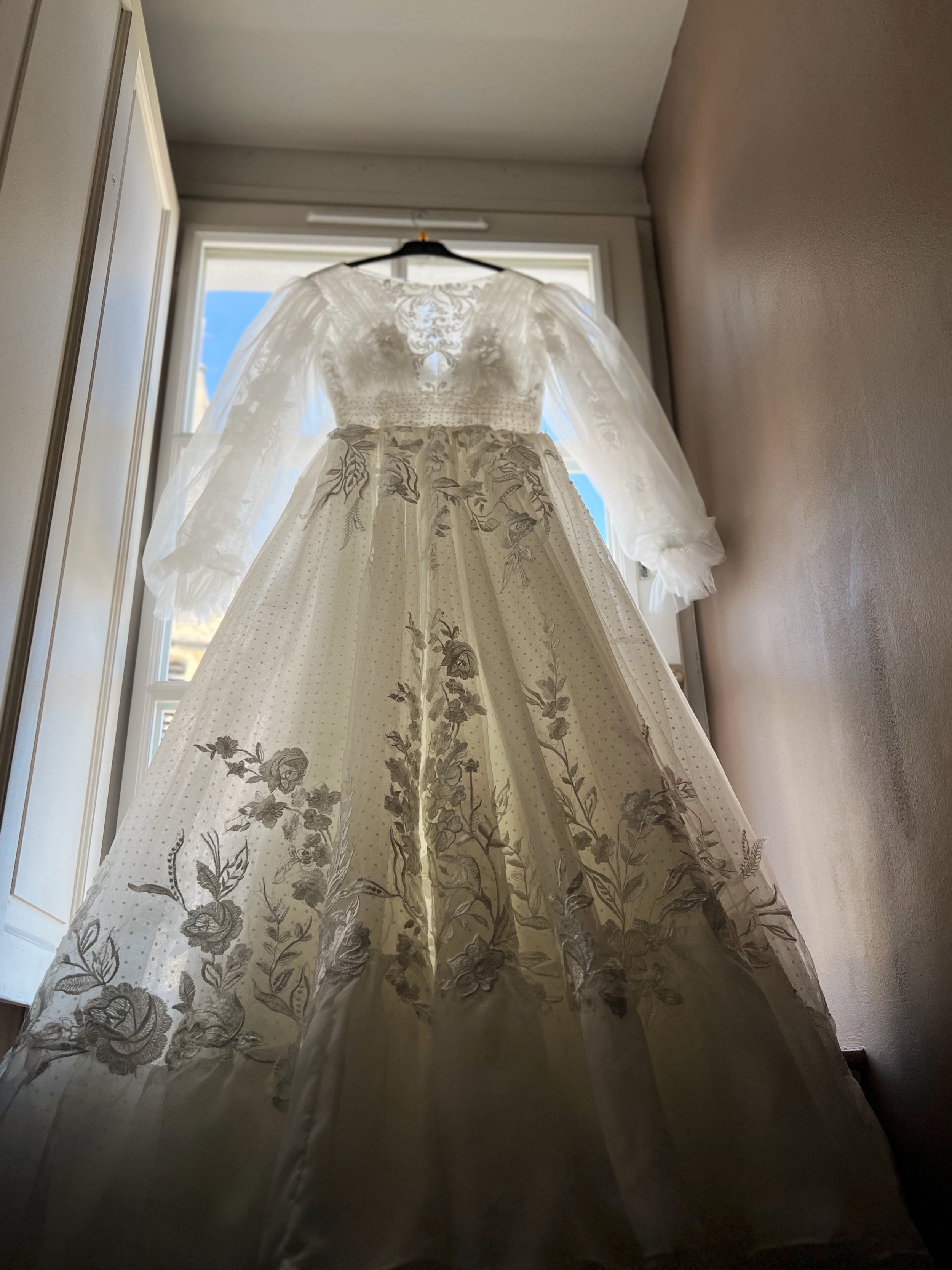 Robe de mariée en dentelle blanche suspendue devant une fenêtre.