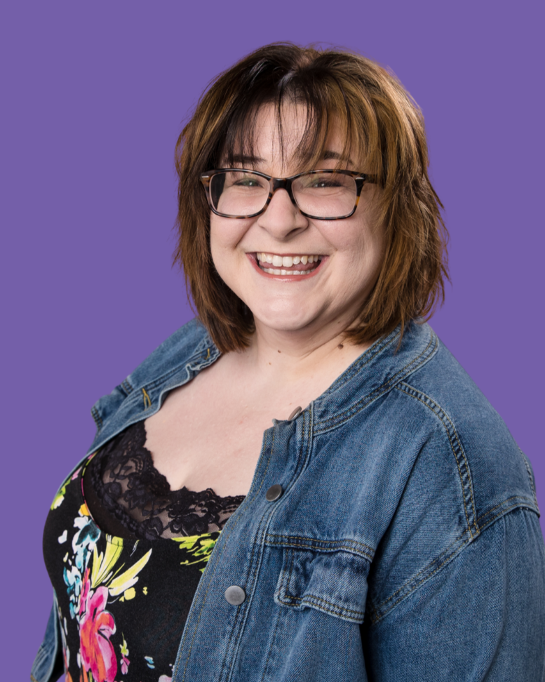 Picture of Lauren with short, brown hair, glasses and bangs, wearing a floral jumper with a jean jacket