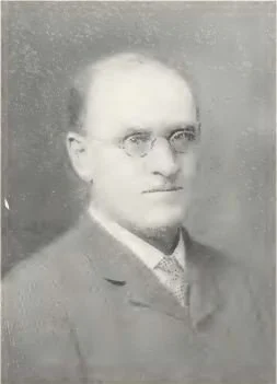 Black and white portrait of a man with glasses wearing a suit and tie, facing forward.