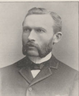 Black and white portrait of a man with a beard, wearing a suit and bow tie, looking to the side.