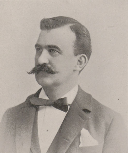 A black-and-white portrait of a man with a mustache and neatly combed hair, dressed in a suit with a bow tie.