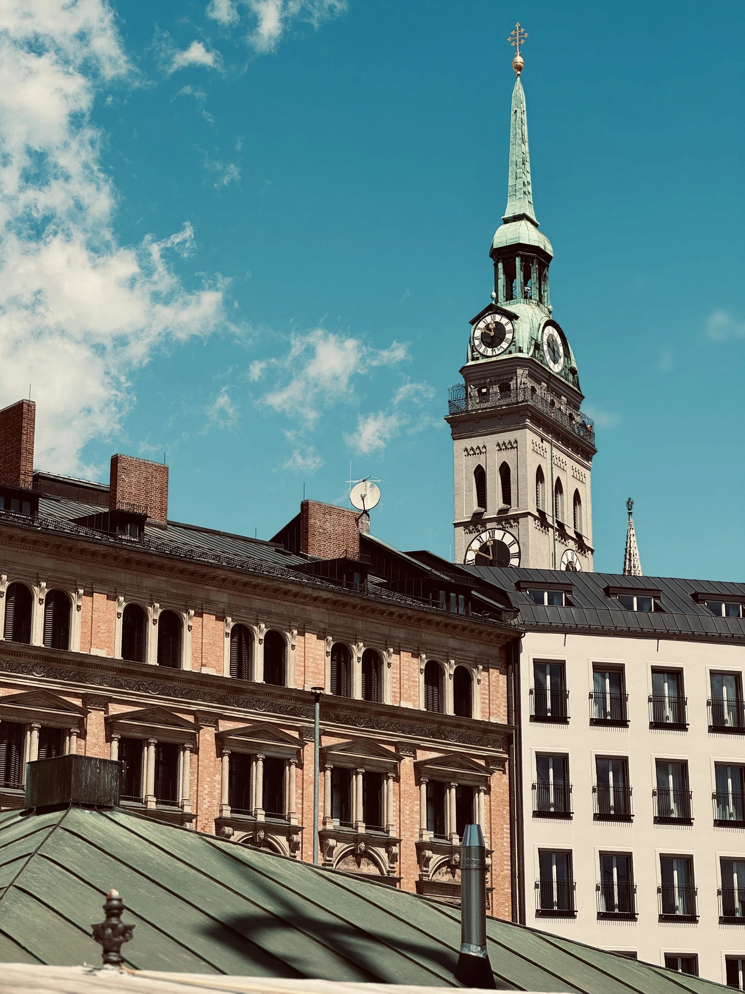 Cityscape with historic clock tower and surrounding buildings under a partly cloudy sky.
