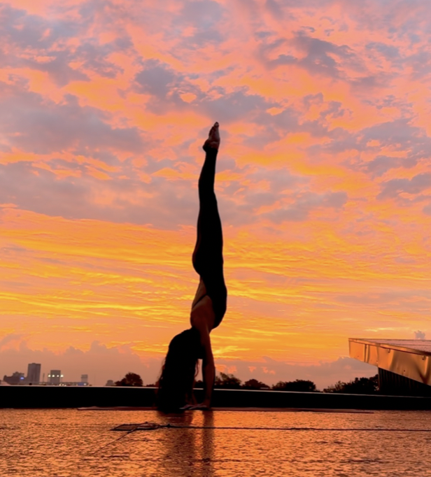 Person performing a handstand at sunset with a colorful sky in the background.