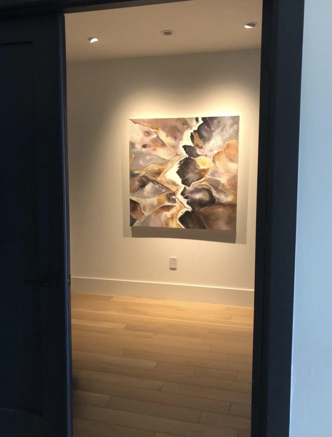 Abstract painting with earthy tones, hanging on a white wall in a gallery space, illuminated by ceiling lights.