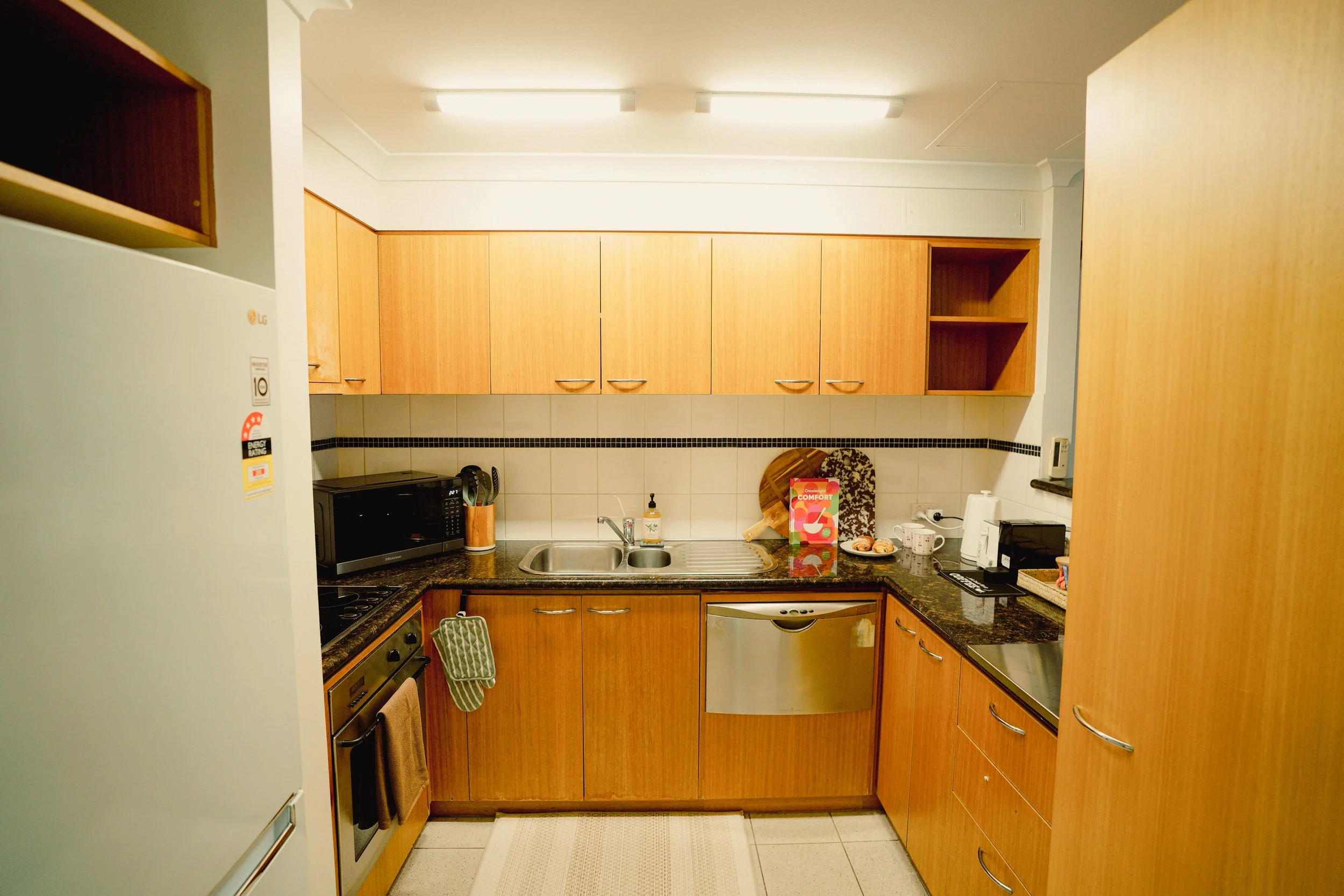 Kitchen countertop with dish drying rack, sink, dishwasher, and potted plant near a window.