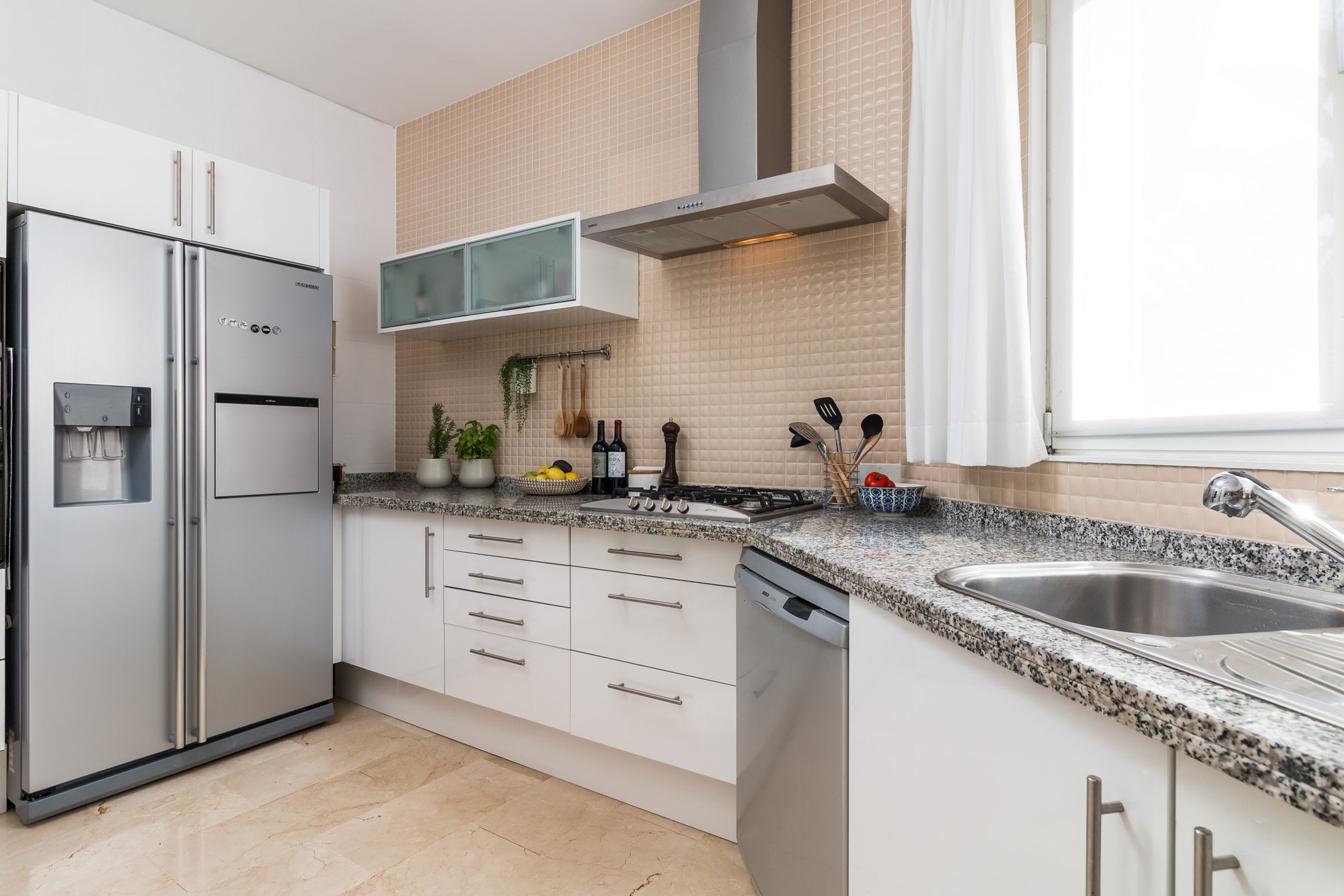 Modern kitchen with stainless steel appliances, white cabinets, granite countertop, and a window with a curtain.