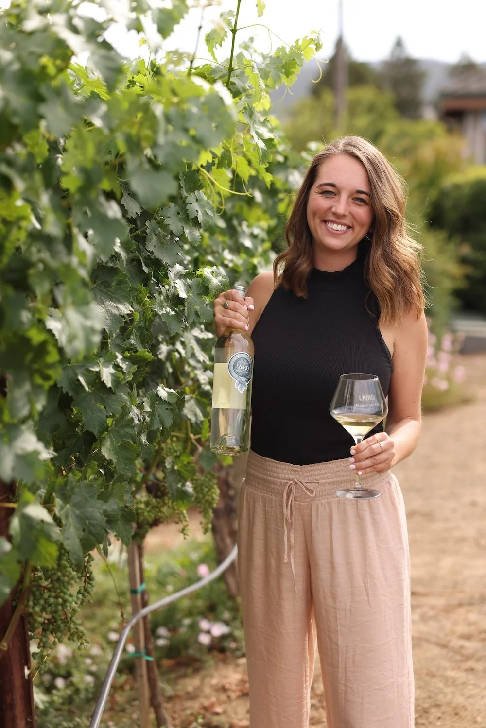 Owner, Maura in Napa Valley holding a wine bottle and glass at Laird Family Winery. Photo by Kenny Kim.