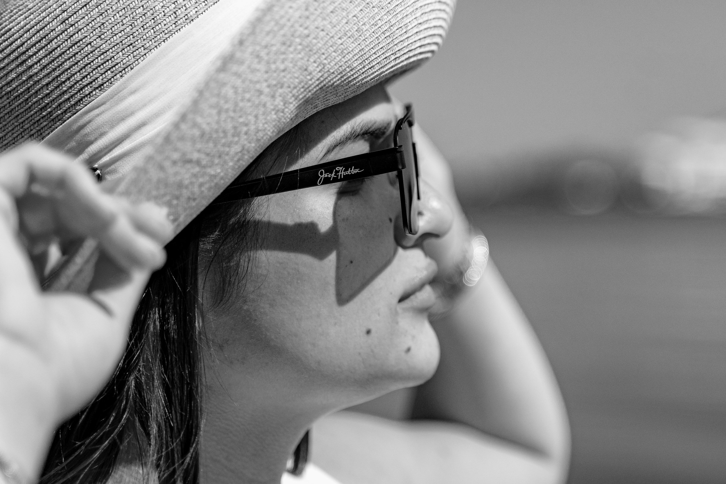 Black and white photo of a person with sunglasses and a woven sun hat, adjusting the hat.