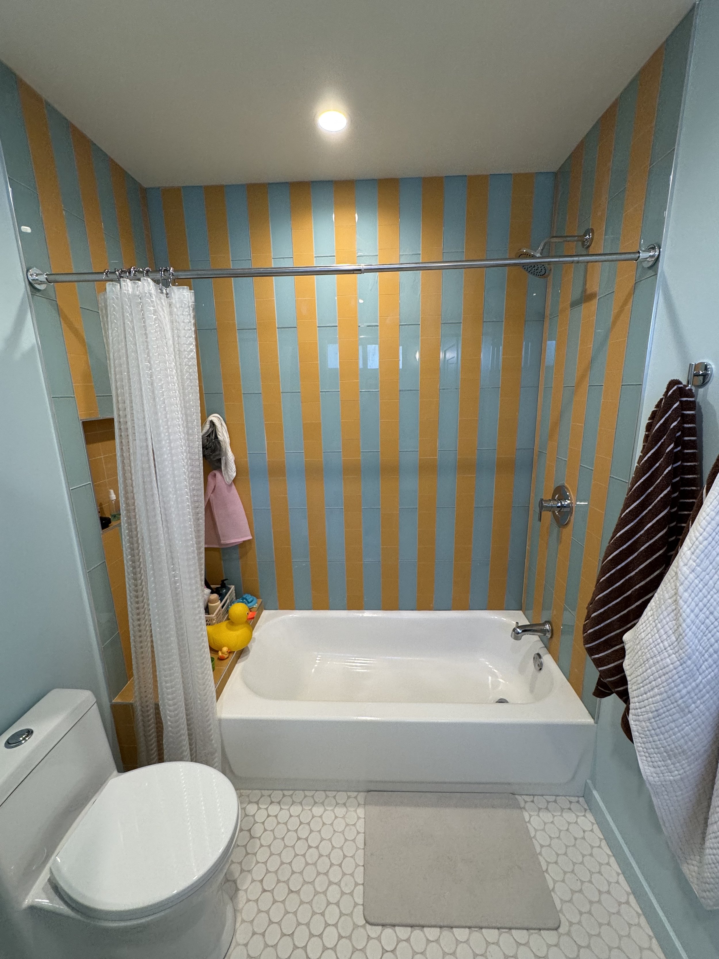 Bathroom with a bathtub, toilet, striped orange and blue tile wall, and towels hanging on hooks.