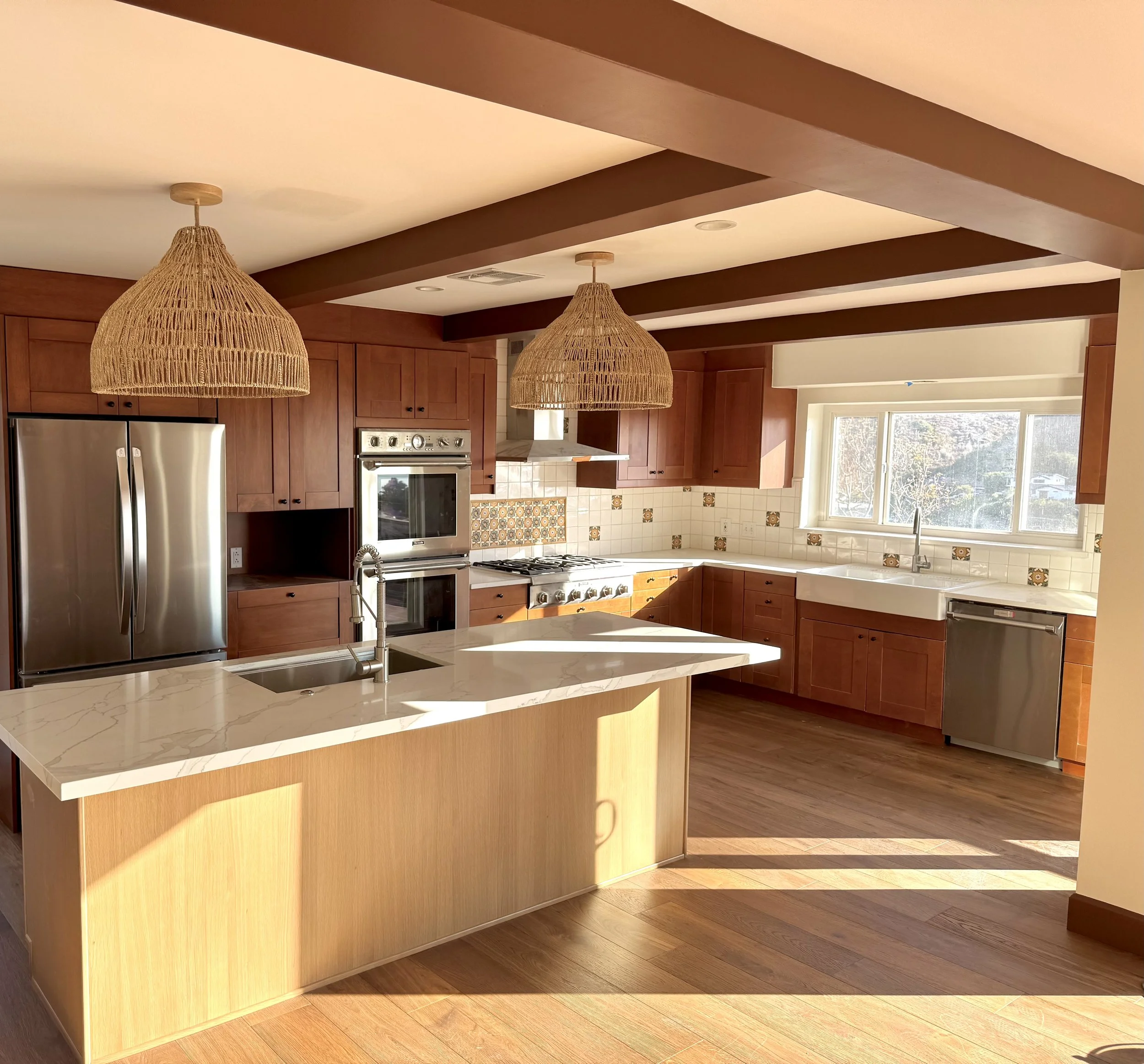 Modern kitchen with wooden cabinets, a white marble island, stainless steel appliances, a large window, and natural sunlight.