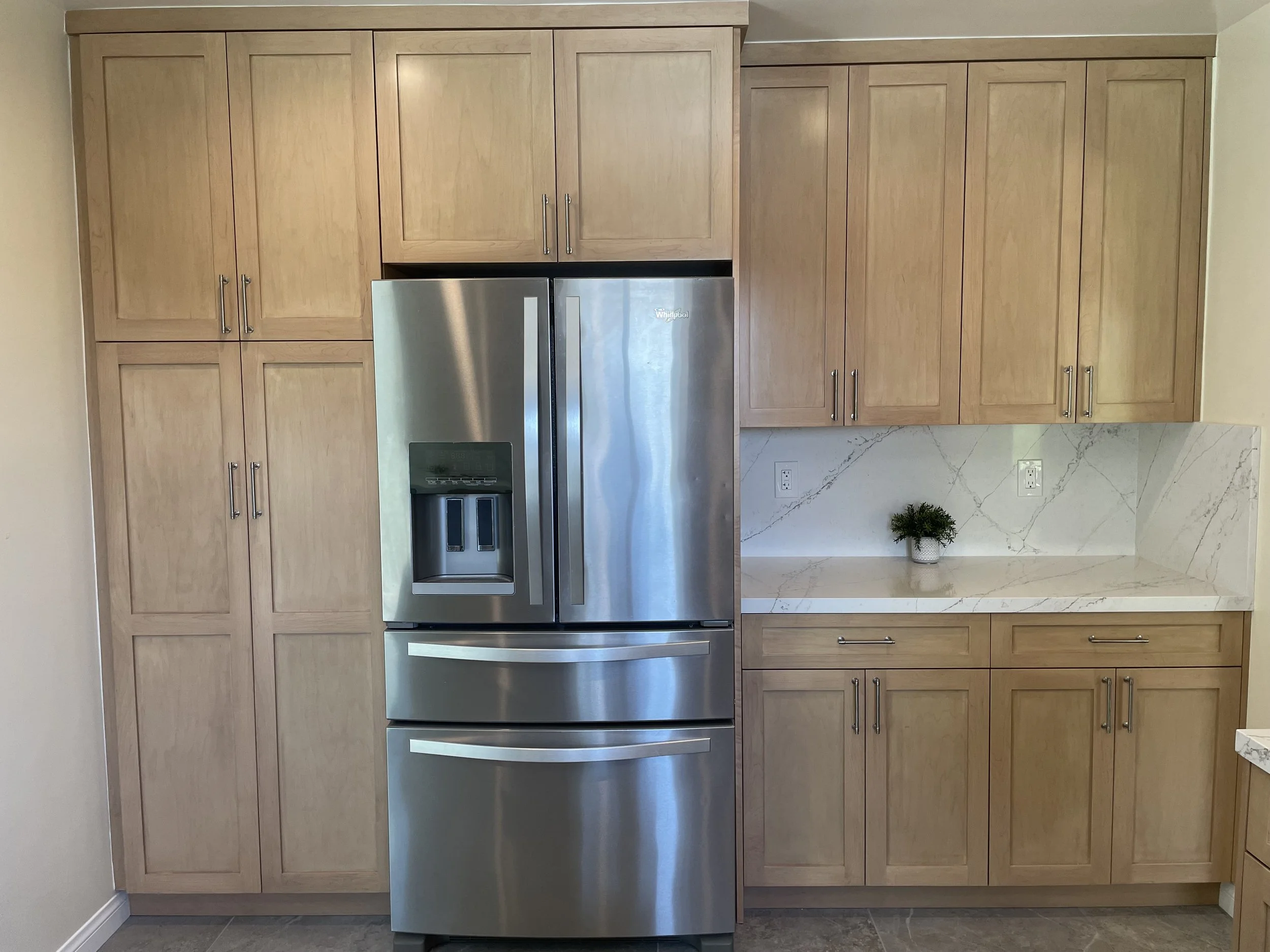 Kitchen with light wood cabinets, a stainless steel refrigerator, and a white marble countertop with a small potted plant.