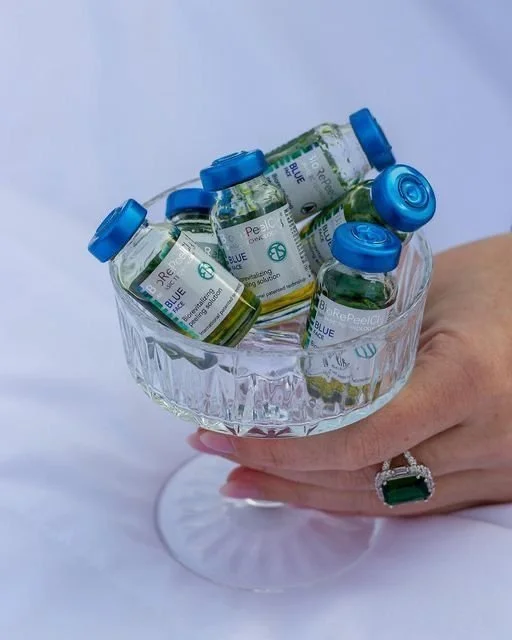 A person's hand holding a clear glass bowl filled with small vials of blue-capped medication or biotech solution.