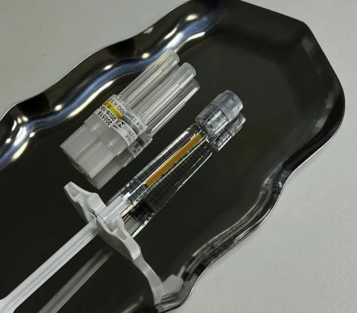 Medical supplies including syringes, a needle, and vials placed on a silver tray.