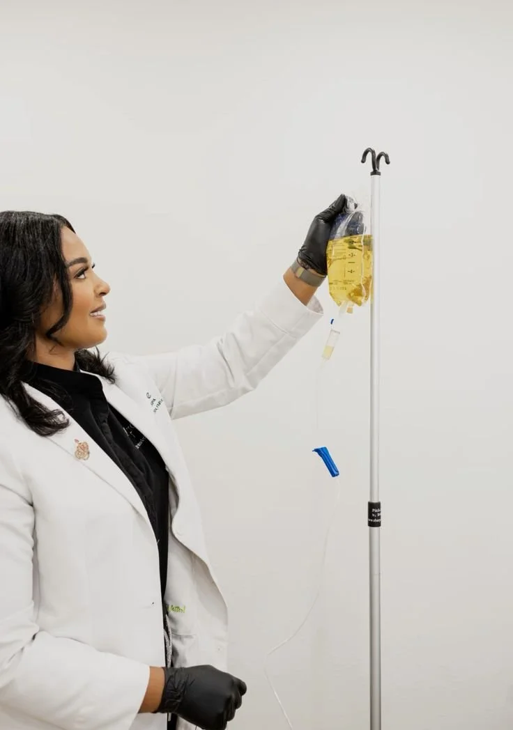 A woman in a white lab coat and black gloves is holding a bag of yellow liquid, connected to IV tubing, during a medical procedure or experiment.
