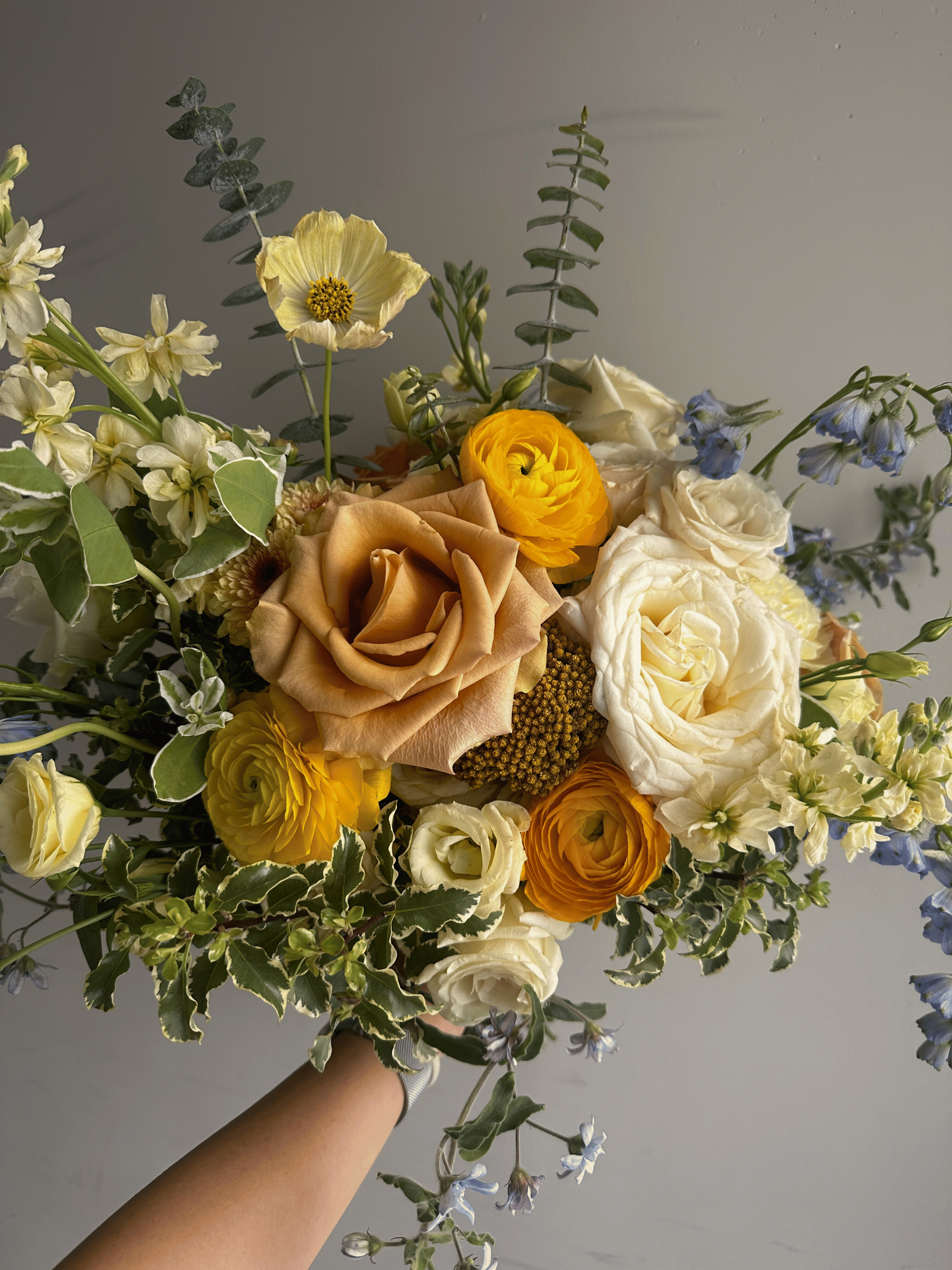 Colorful bouquet with yellow and white roses, blue delphiniums, and greenery