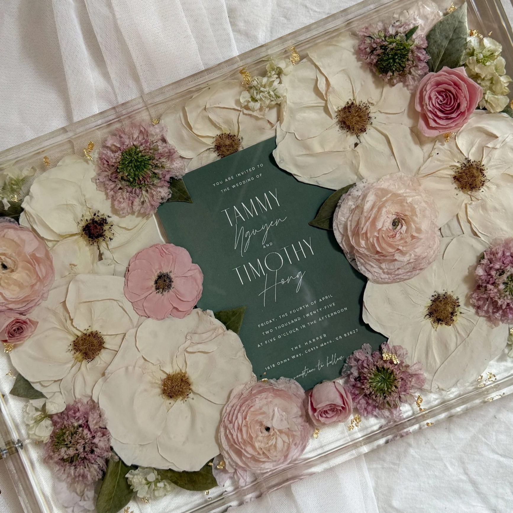 11-by-17-inch acrylic tray preserving blush, ivory, and white wedding flowers around the client’s dark green wedding invitation