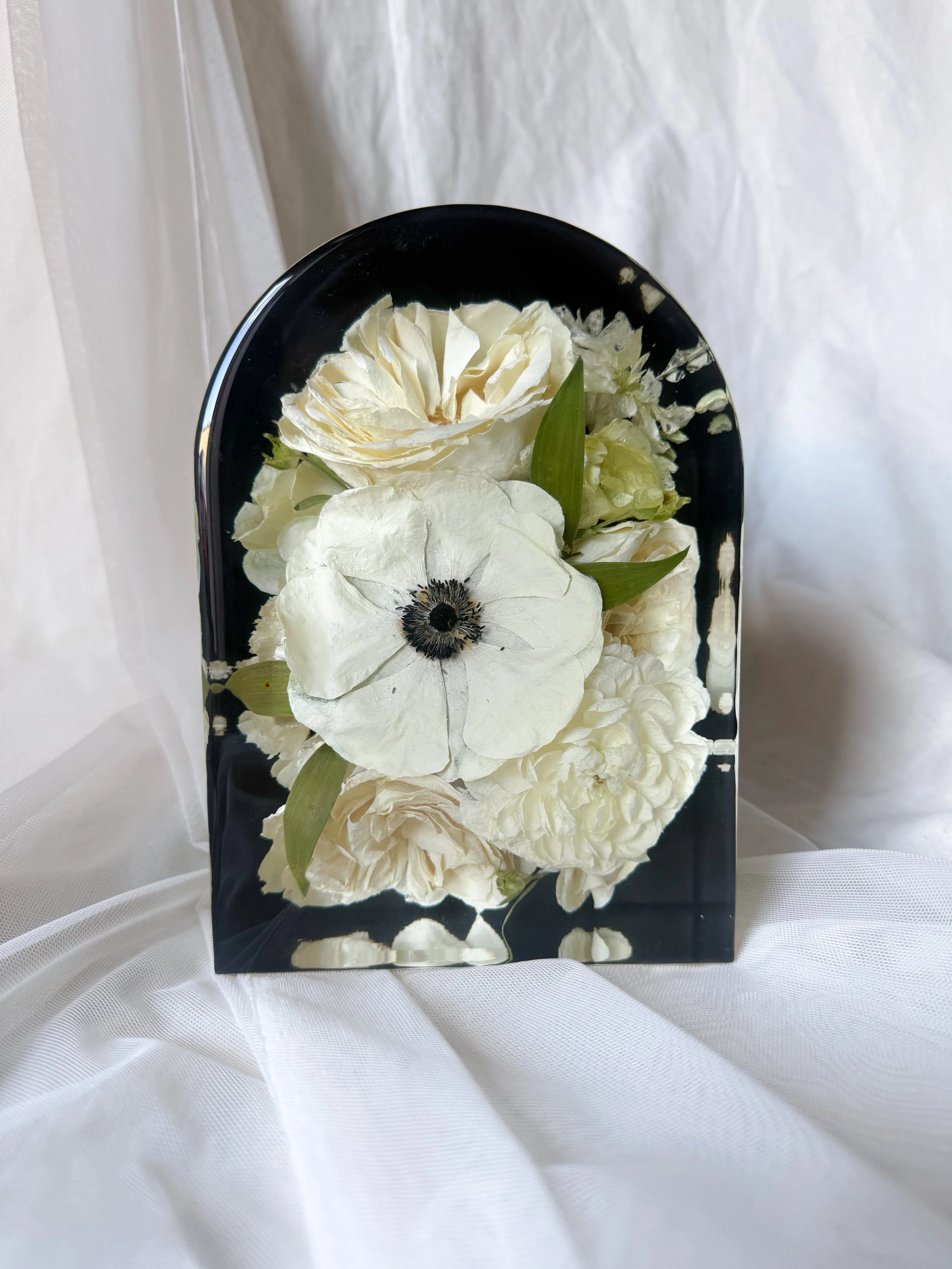 Black 5-by-7-inch resin arch preserving ivory roses, a white anemone, and other white flowers with greenery