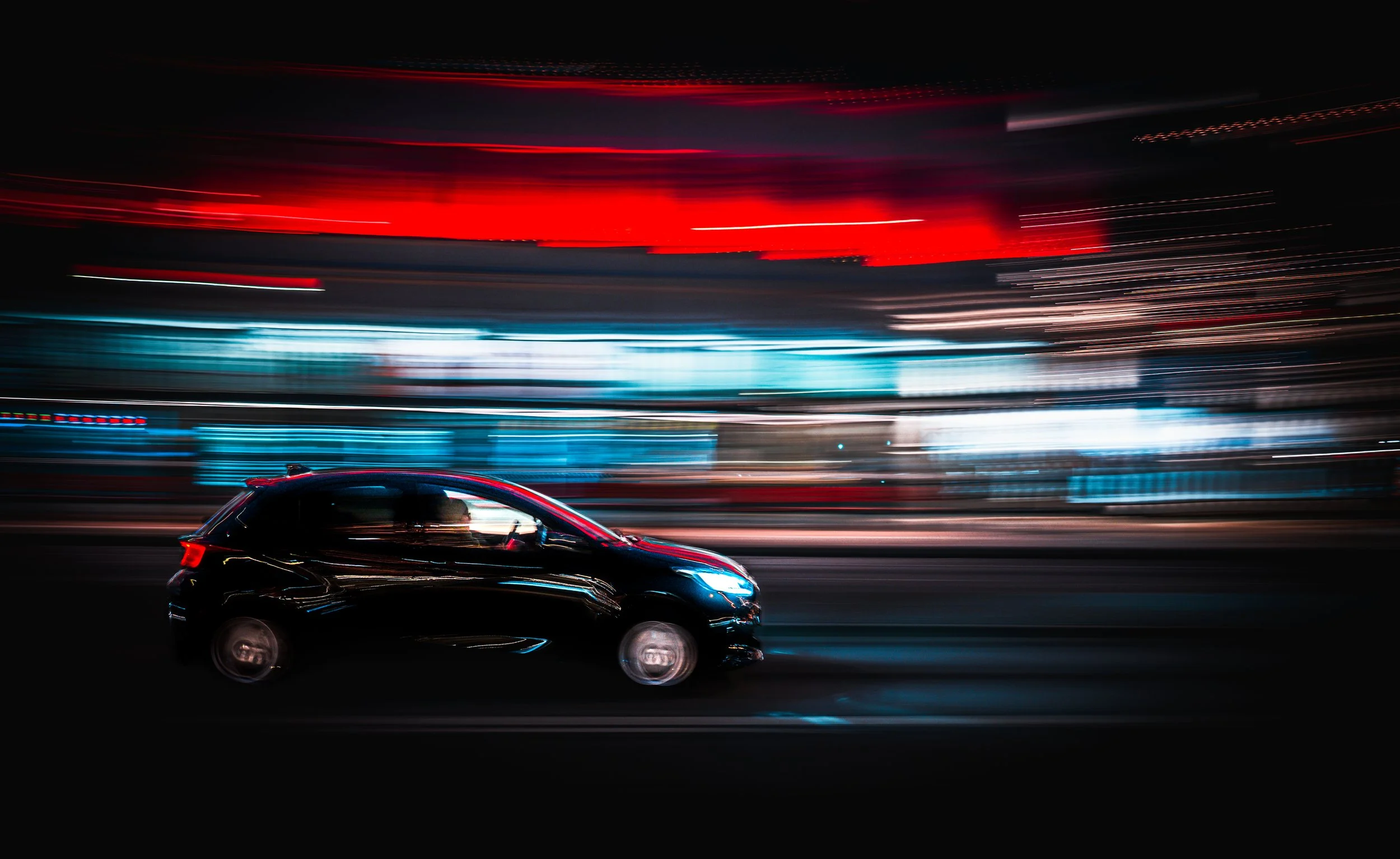 A black car moving at night with colorful light streaks in the background.  THE ART OF PHOTOGRAPHY